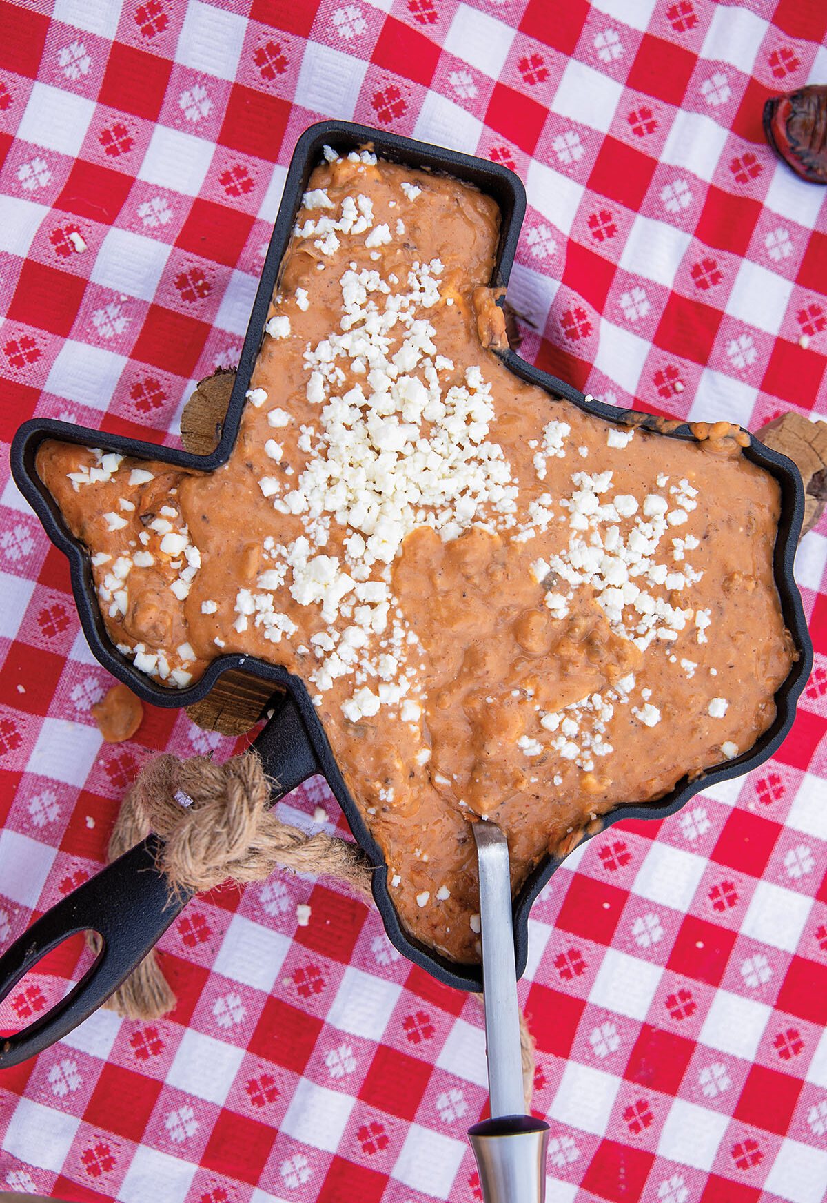 An overhead view of orange-brown queso topped with white crumbled cheese in a Texas-shaped cast iron skillet