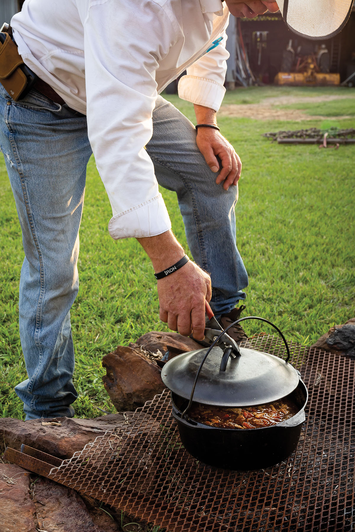 A man in a white shirt leans over a cast-iron cook pot