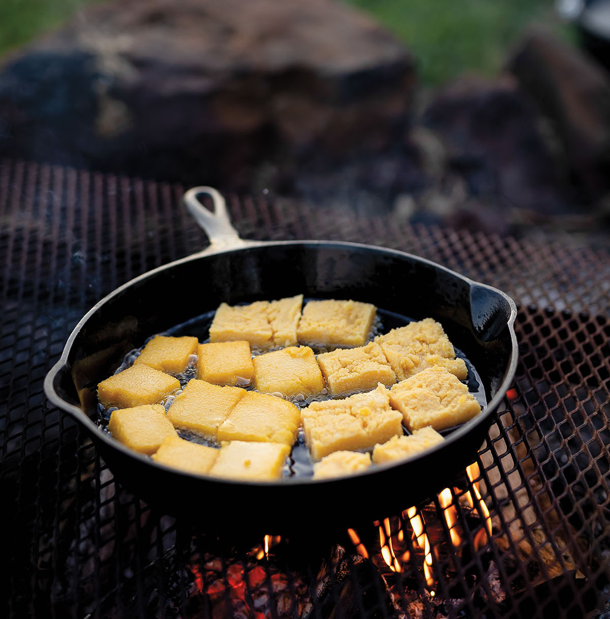 Squares of yellow corn frying in a black cast iron skillet over a fire