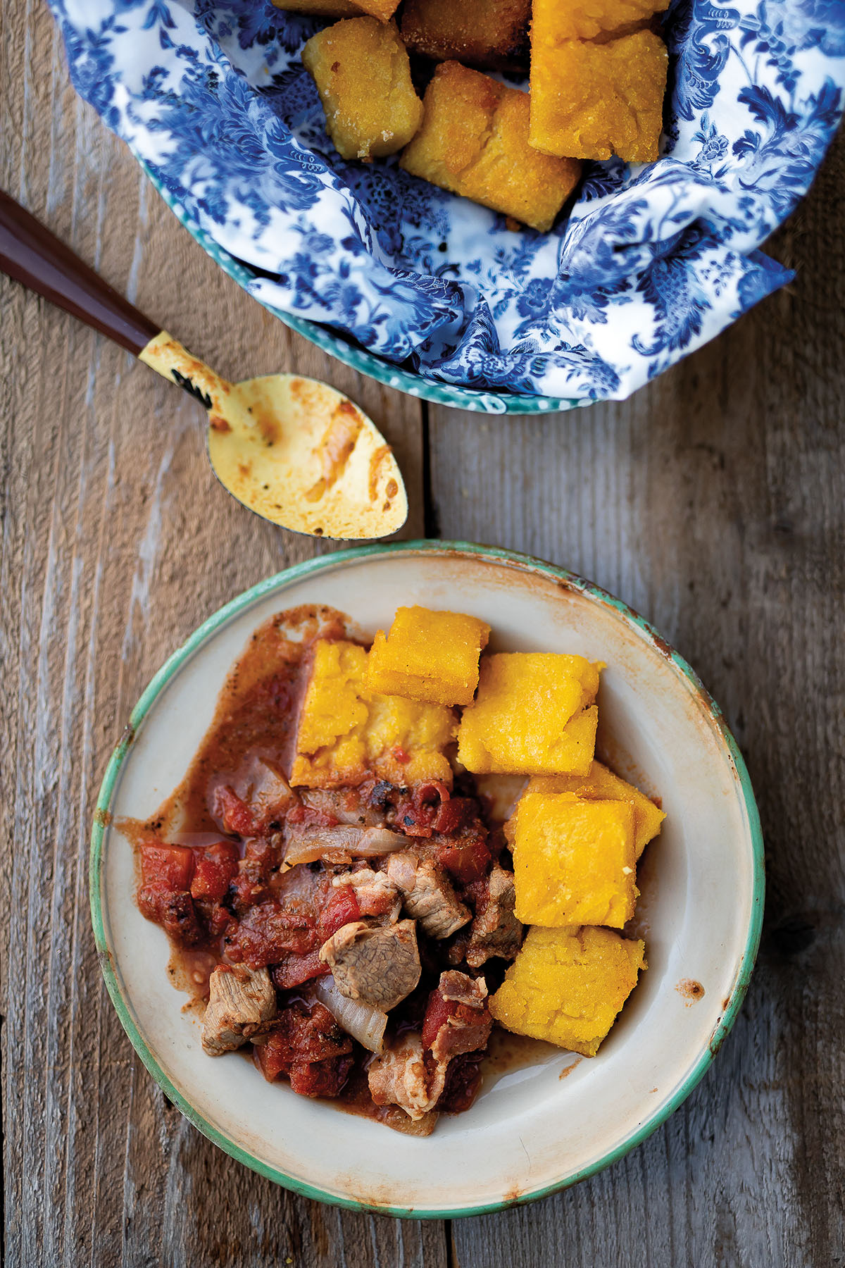 An overhead view of corn dodgers served with a meat stew on a stone plate next to a white and blue dish