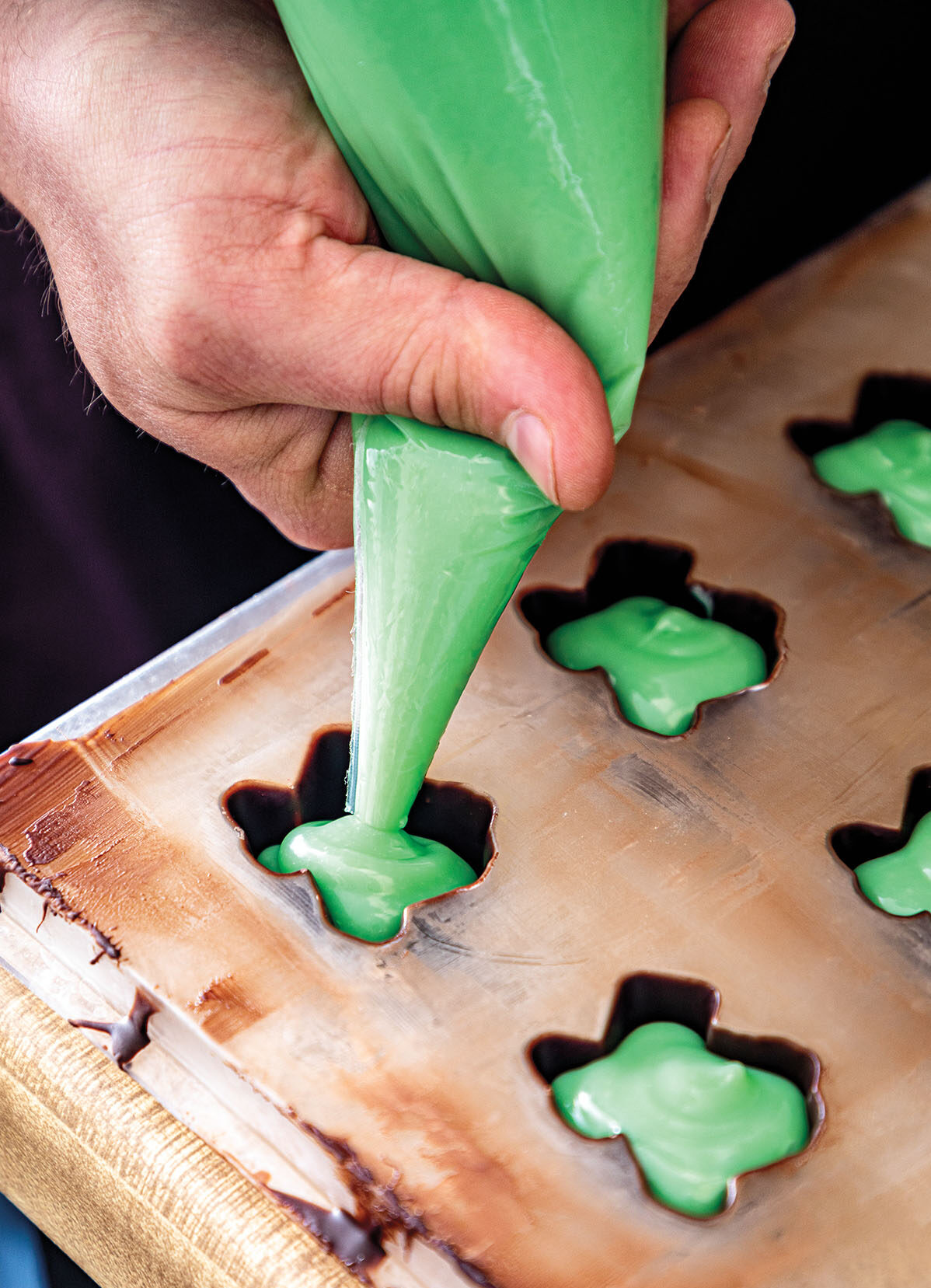 A green piping bag fills texas-shaped molds with green chocolate