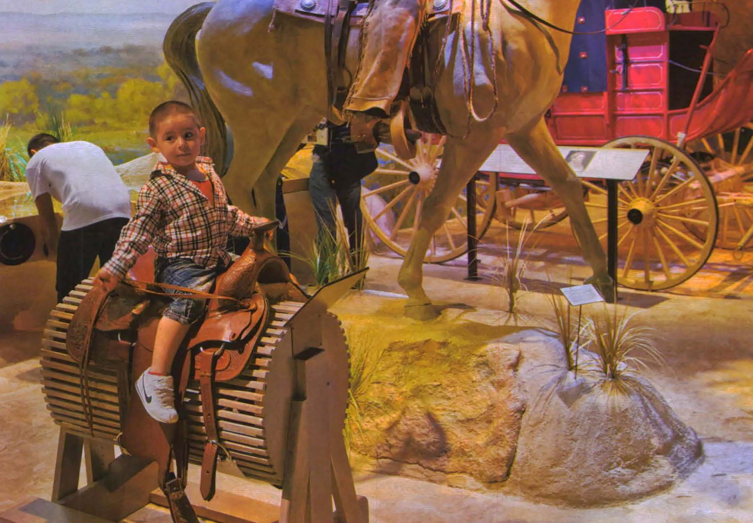 A child sits on a saddle in front of a statue