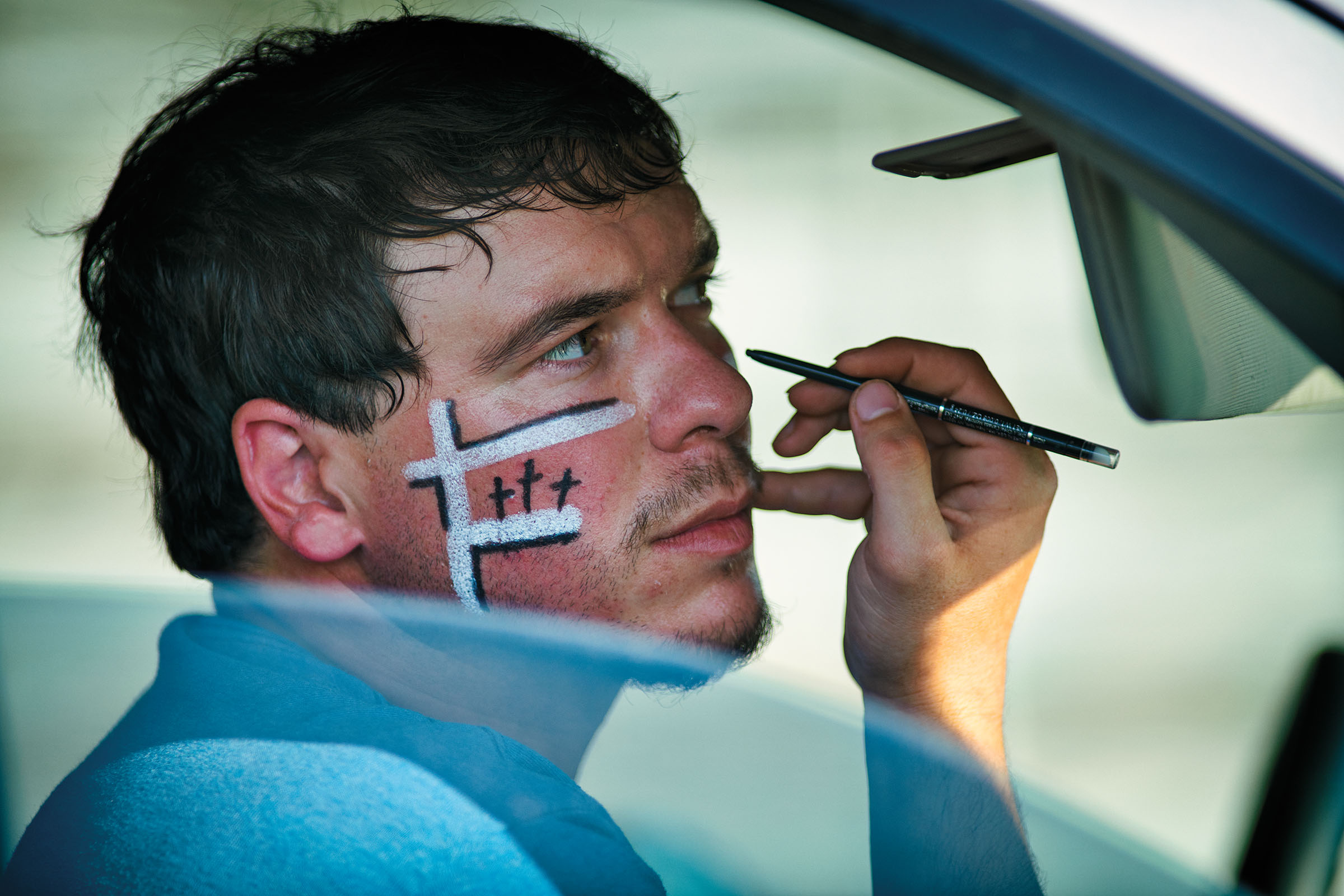A man looks straight ahead as a small paintbrush applies paint to his nose area