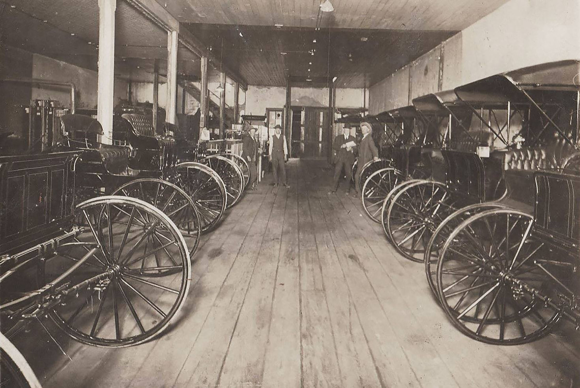 A view down a large room with wood plank floors lined on both sides with buggies