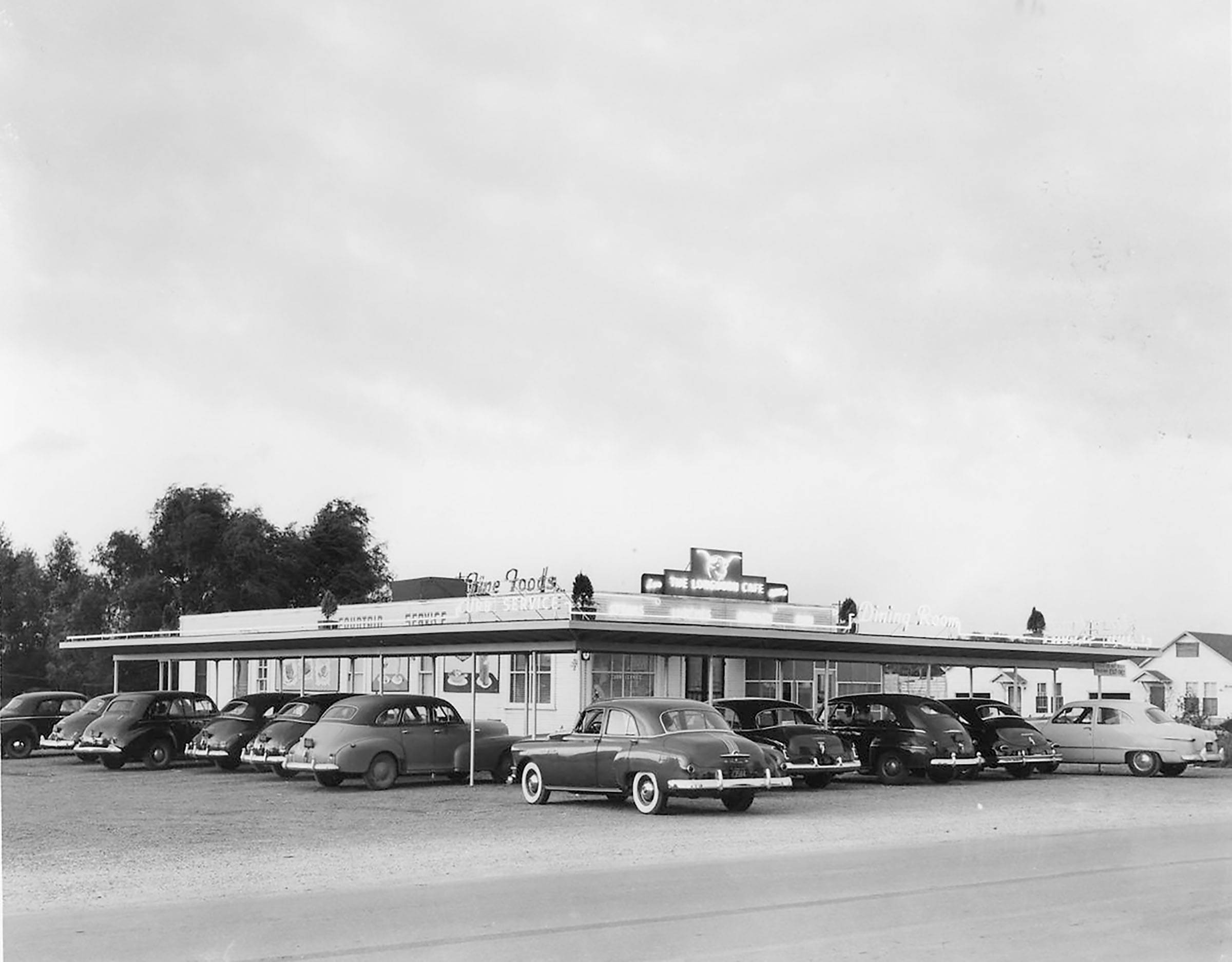 Large black cars parked outside of a white cafe
