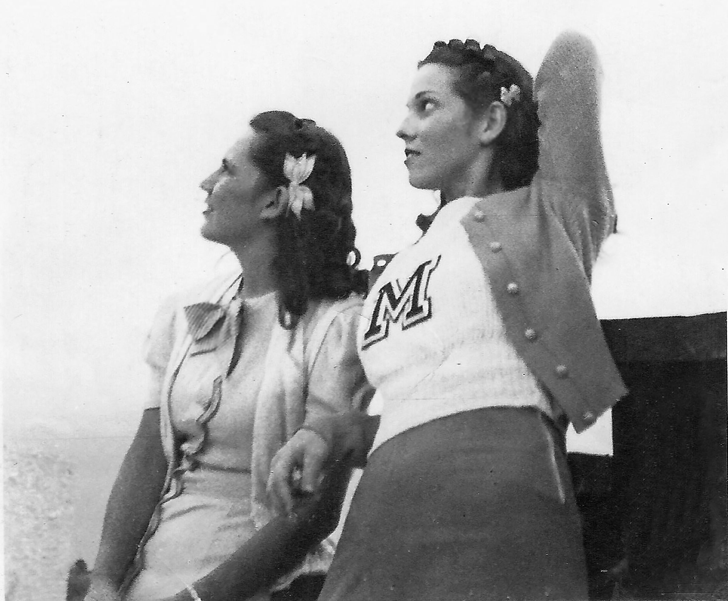 Two women in cheerleading uniforms stand next to football bleachers