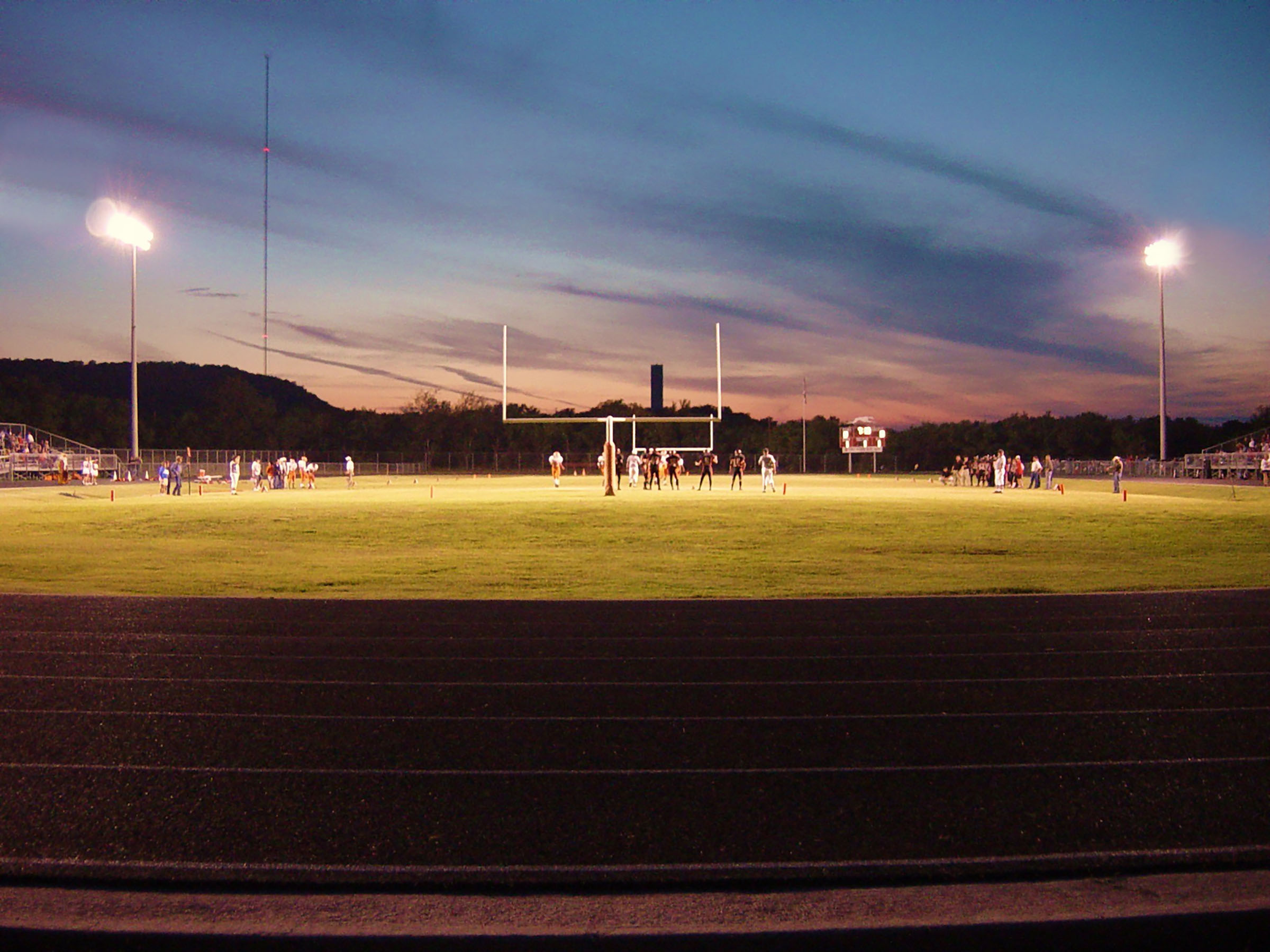 A blue and pink sunset over a green, lit up football field where a small group of players play