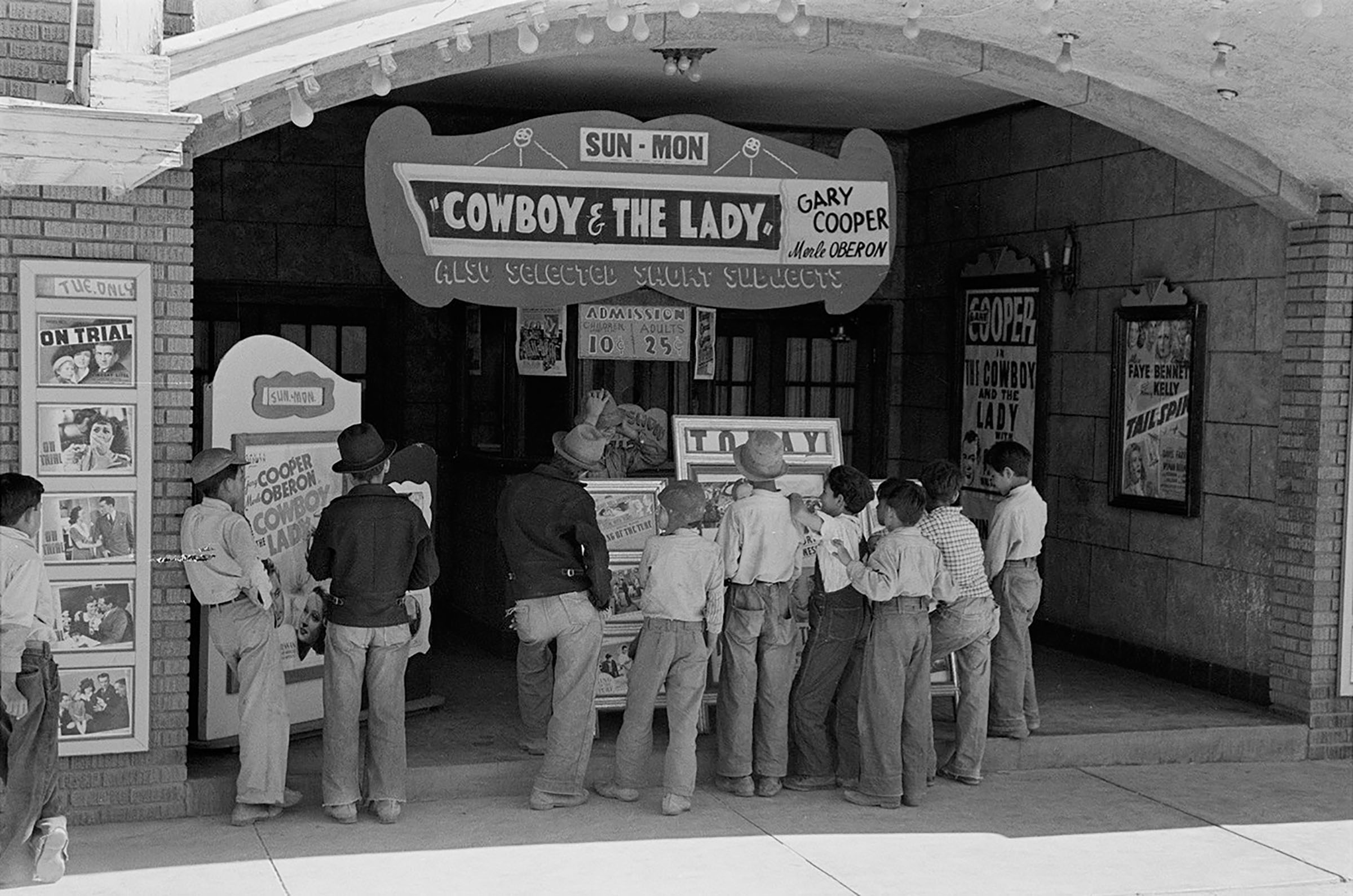 A group of young people line up for a theater box office under a sign reading 'Cowboy & The Lady'