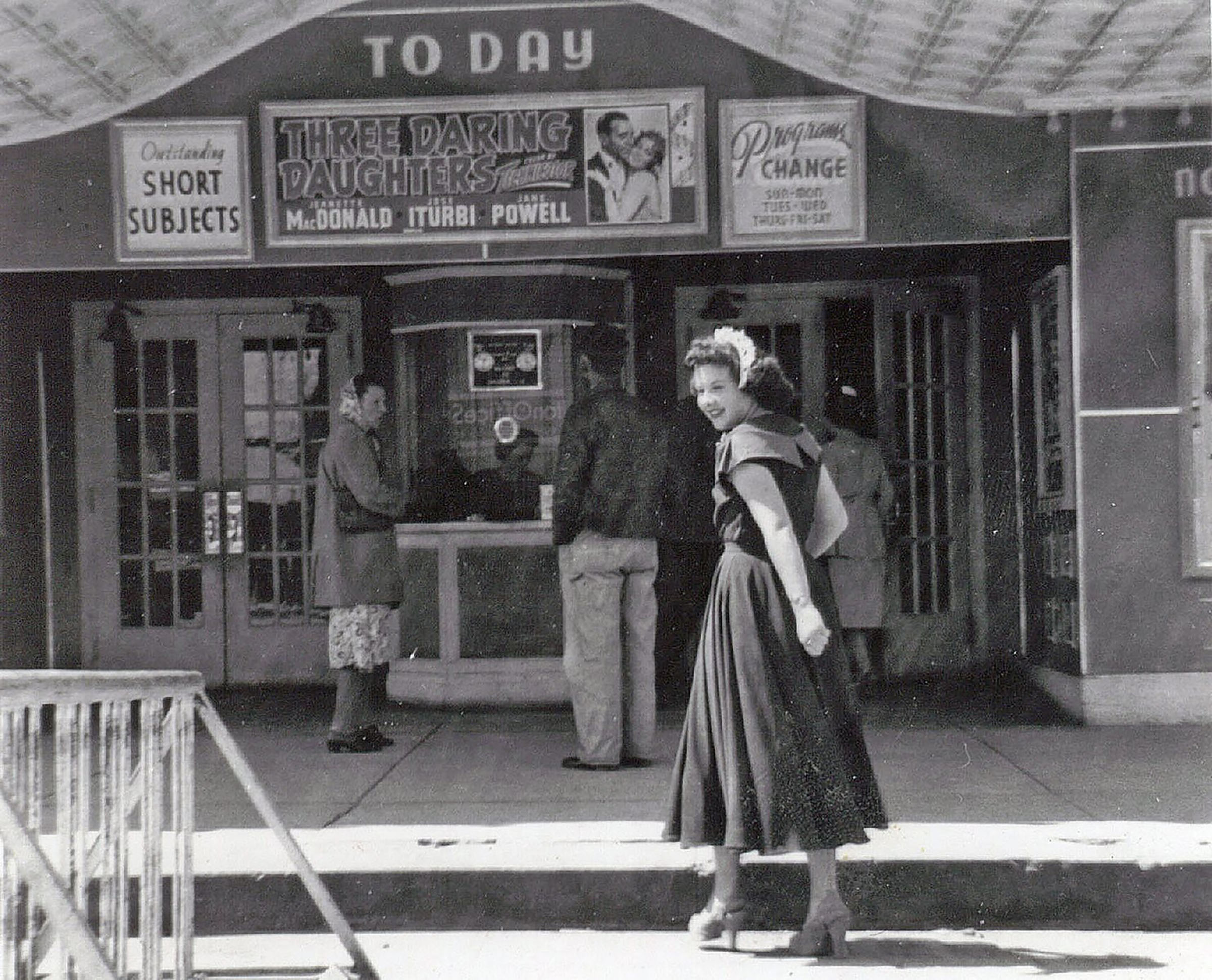 A woman in a dark dress and white headband walks toward a theater entrance