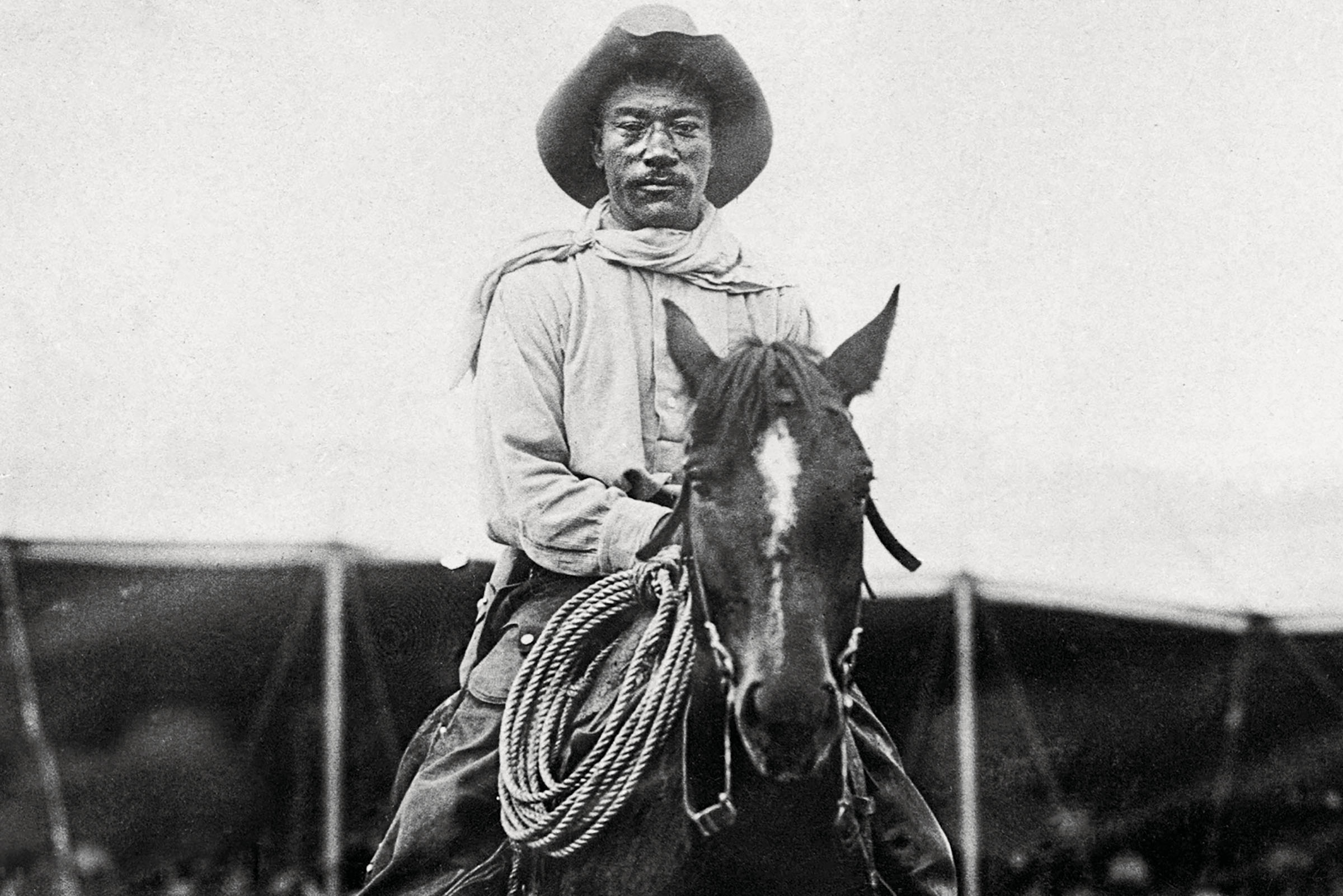 A man in a cowboy hat sits atop a horse in a black and white photo