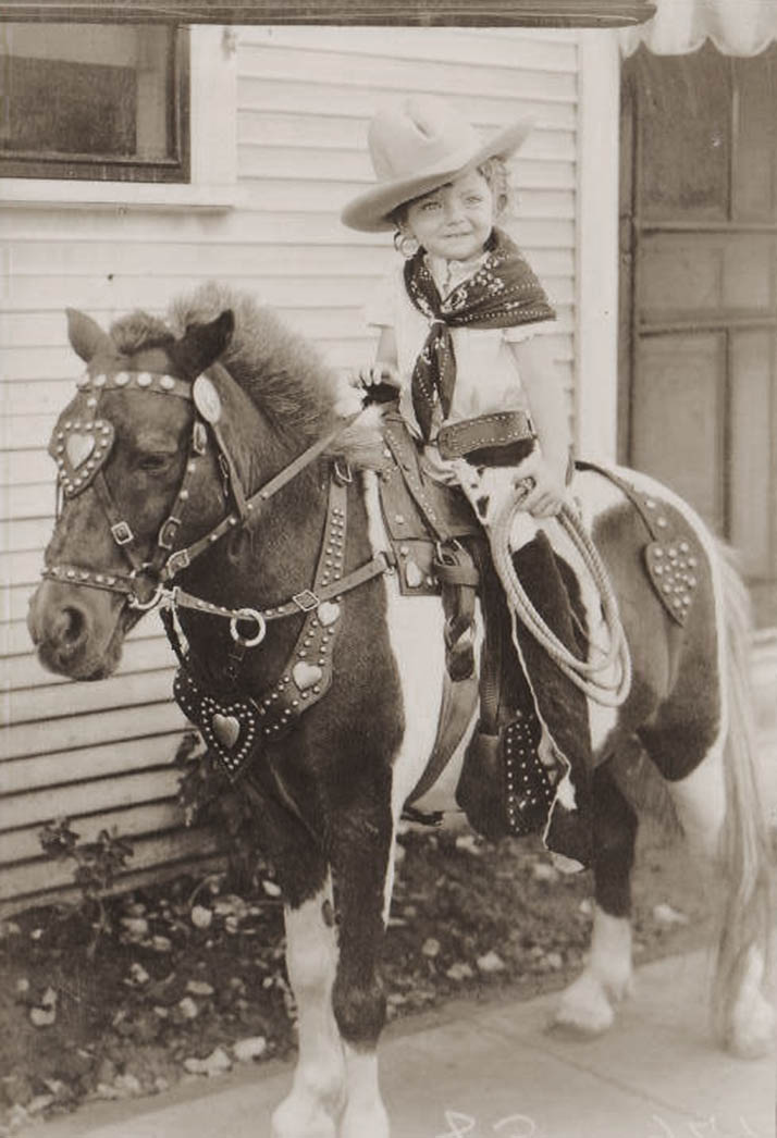 A young woman sits atop a well-decorated horse in cowboy attire