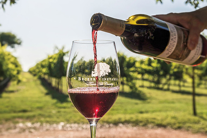 Red wine is poured from a bottle into a clear glass reading "Becker Vineyards"