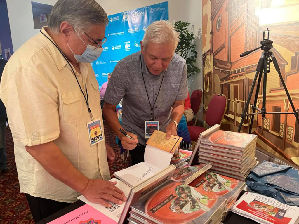 Stacks of books sit on a table where author and chef Adán Medrano signs a copy of his book at the Guadalupe Latino Bookstore sneak preview event. Photo by Tony Diaz. 