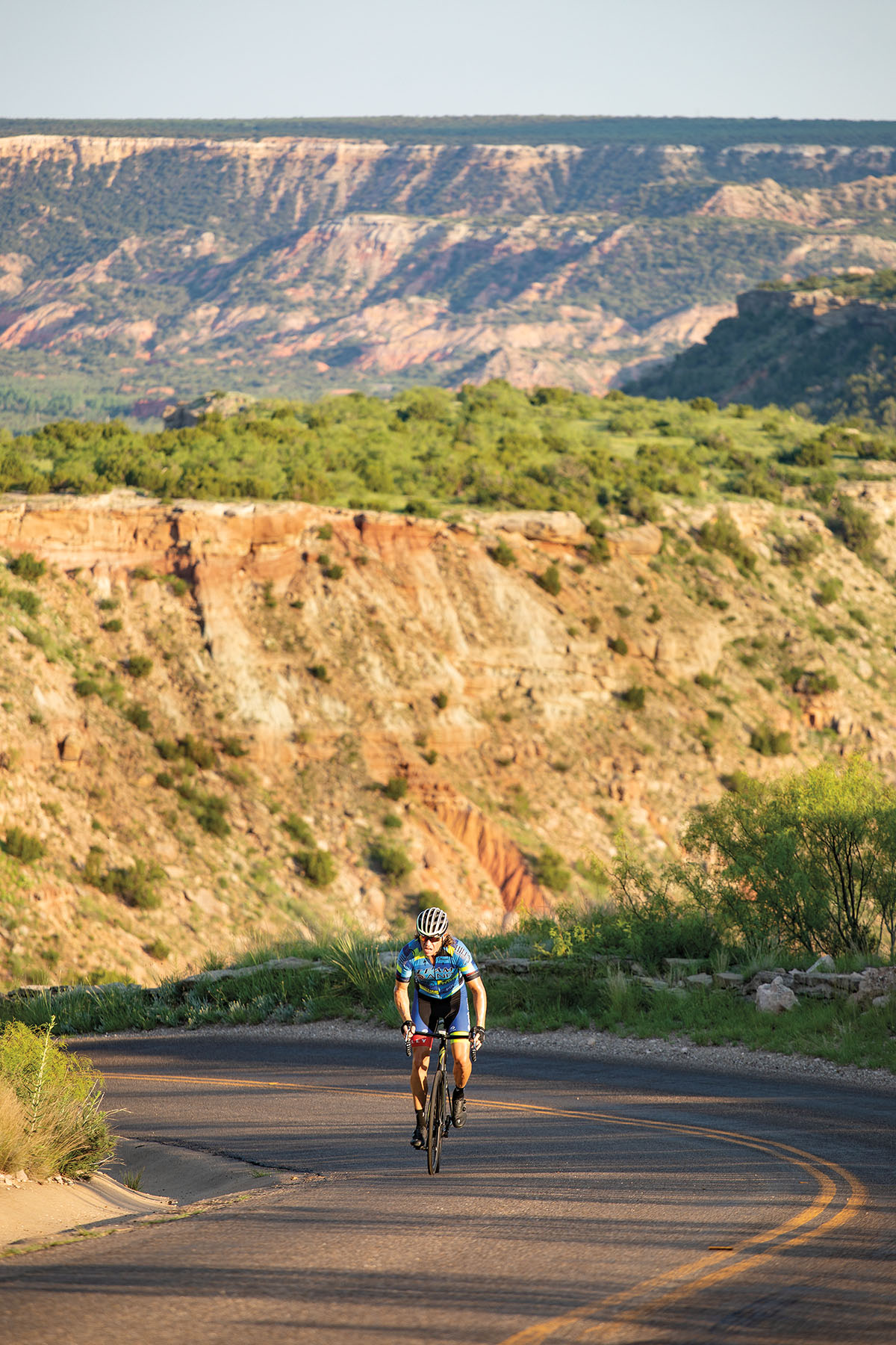 A person rides a bicycle up a hill with large red and green canyons in the background