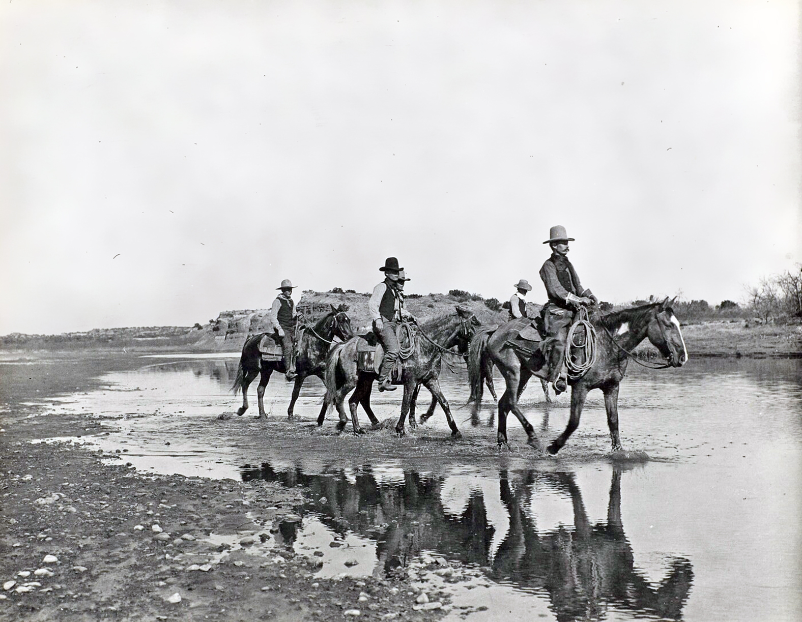 A black and white picture of a group of men on horses on a desert landscape
