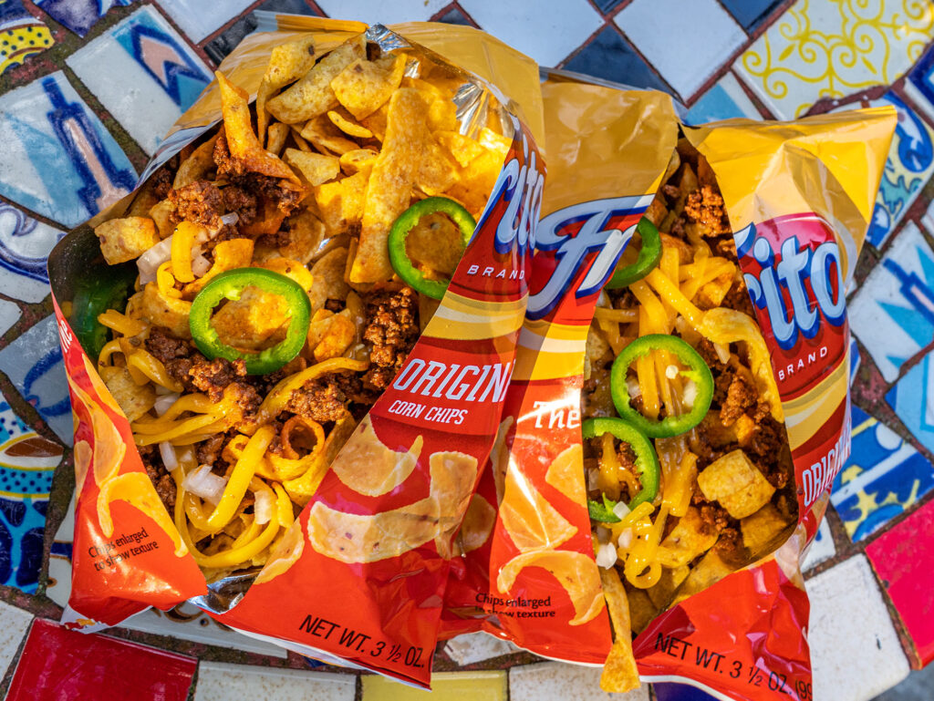 An overhead view of frito bags sliced down the middle and topped with ground beef, onion, cheese and jalapeno slices