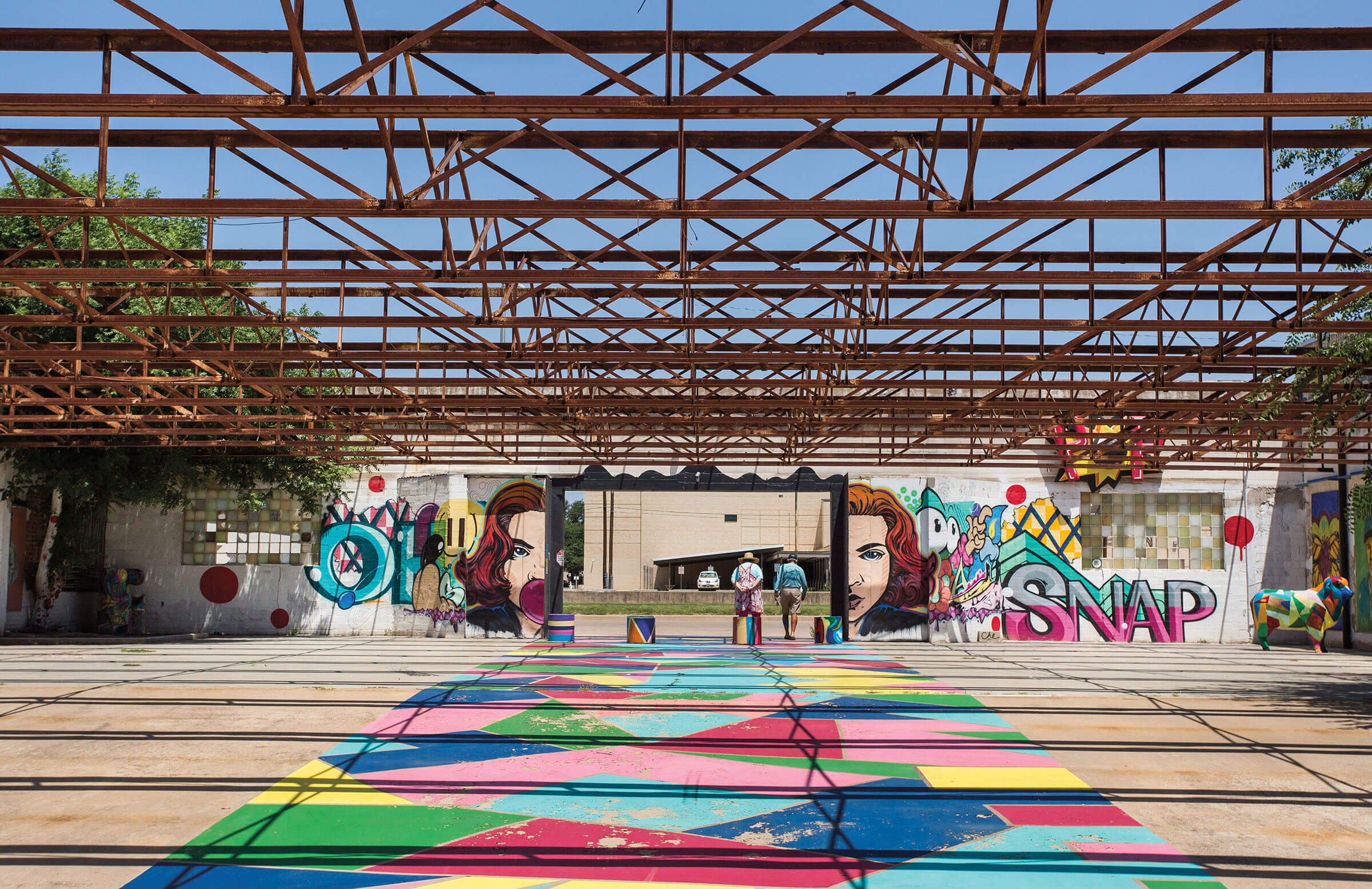A brightly-colored mural and painted concerete floor underneath rusted, open-air rafters