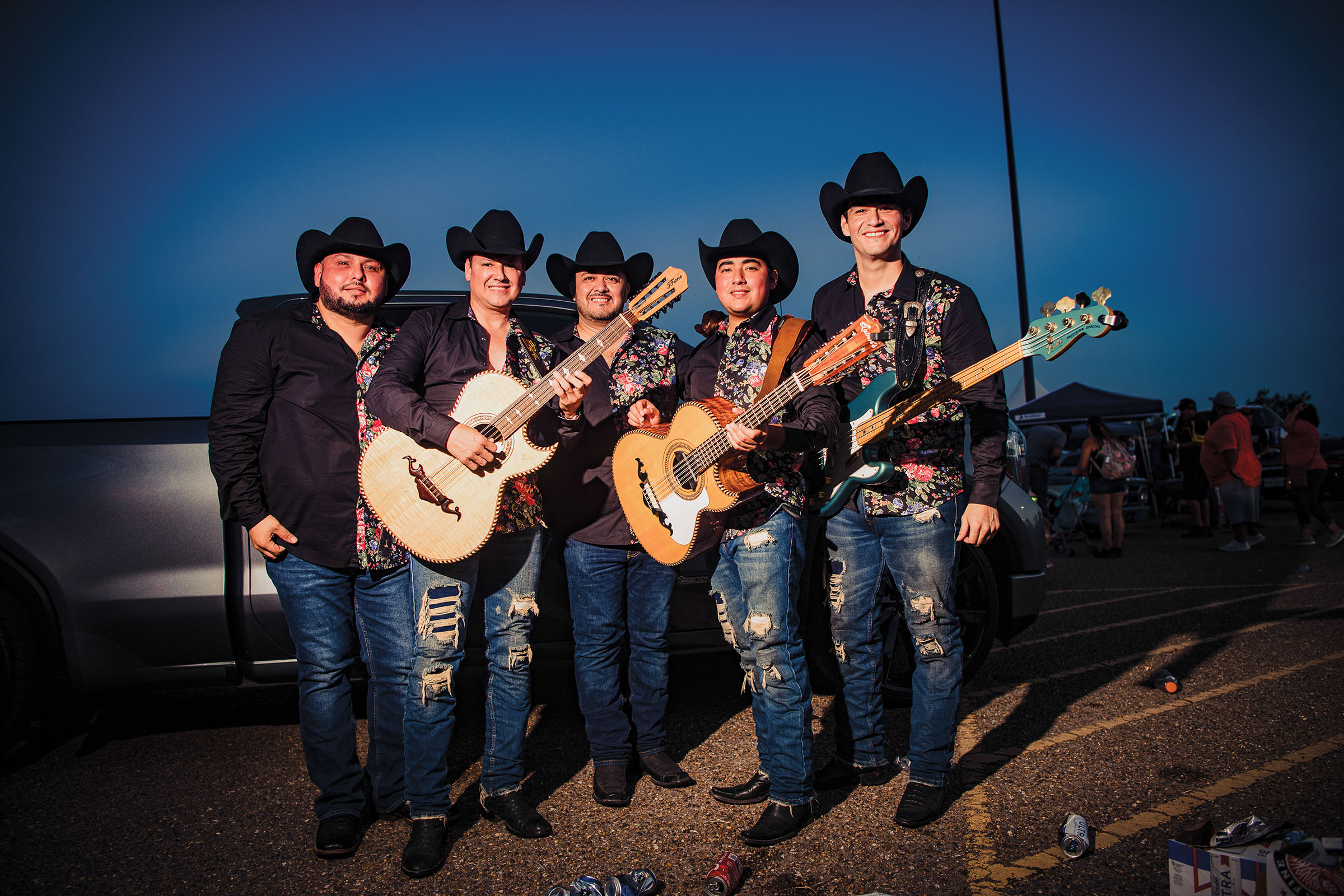 A group of men in jeans and black cowboy hats stand in front of a dark blue evening sky