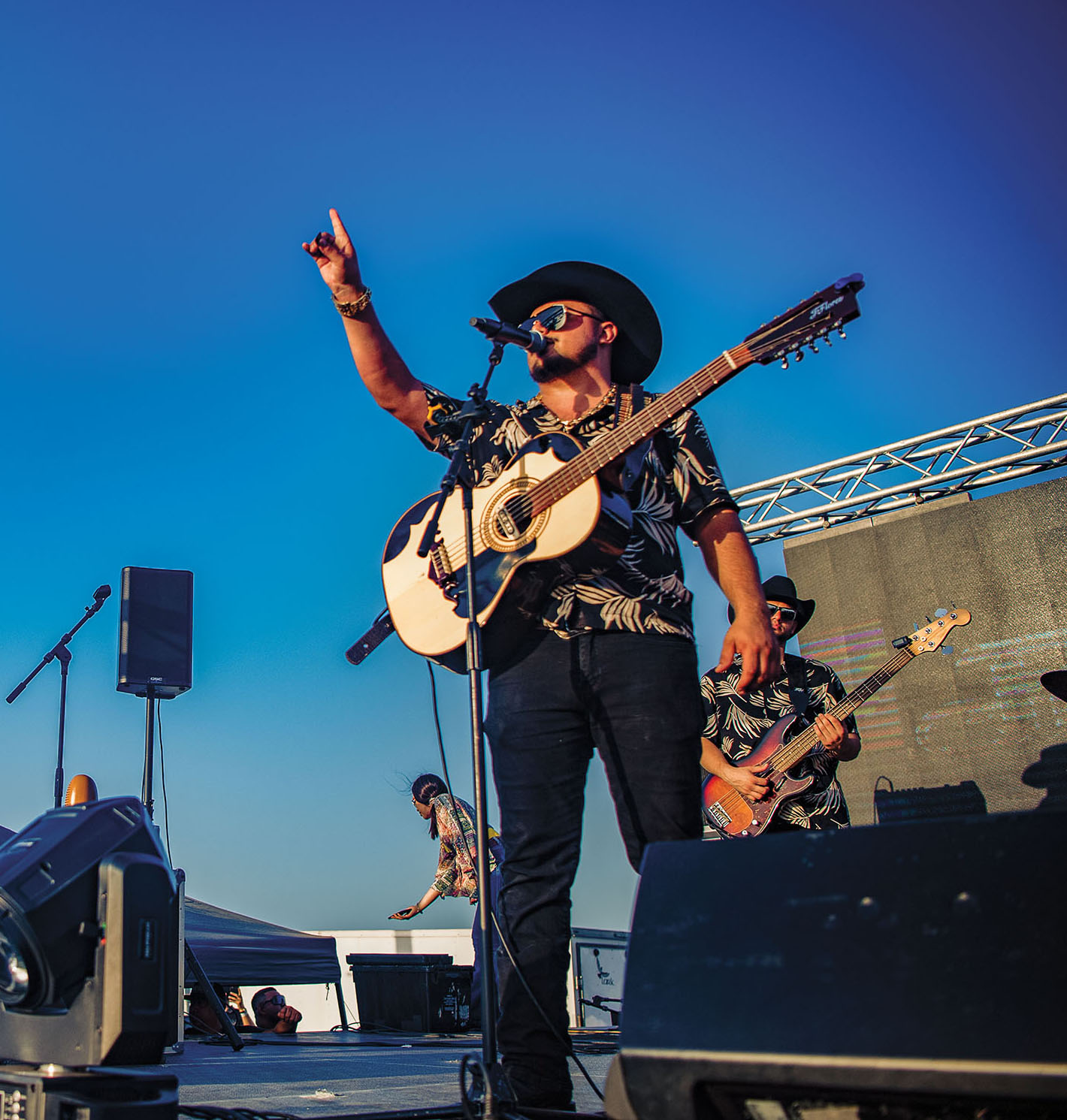 A man in a cowboy hat holds his arm up in front of a crowd with a guitar