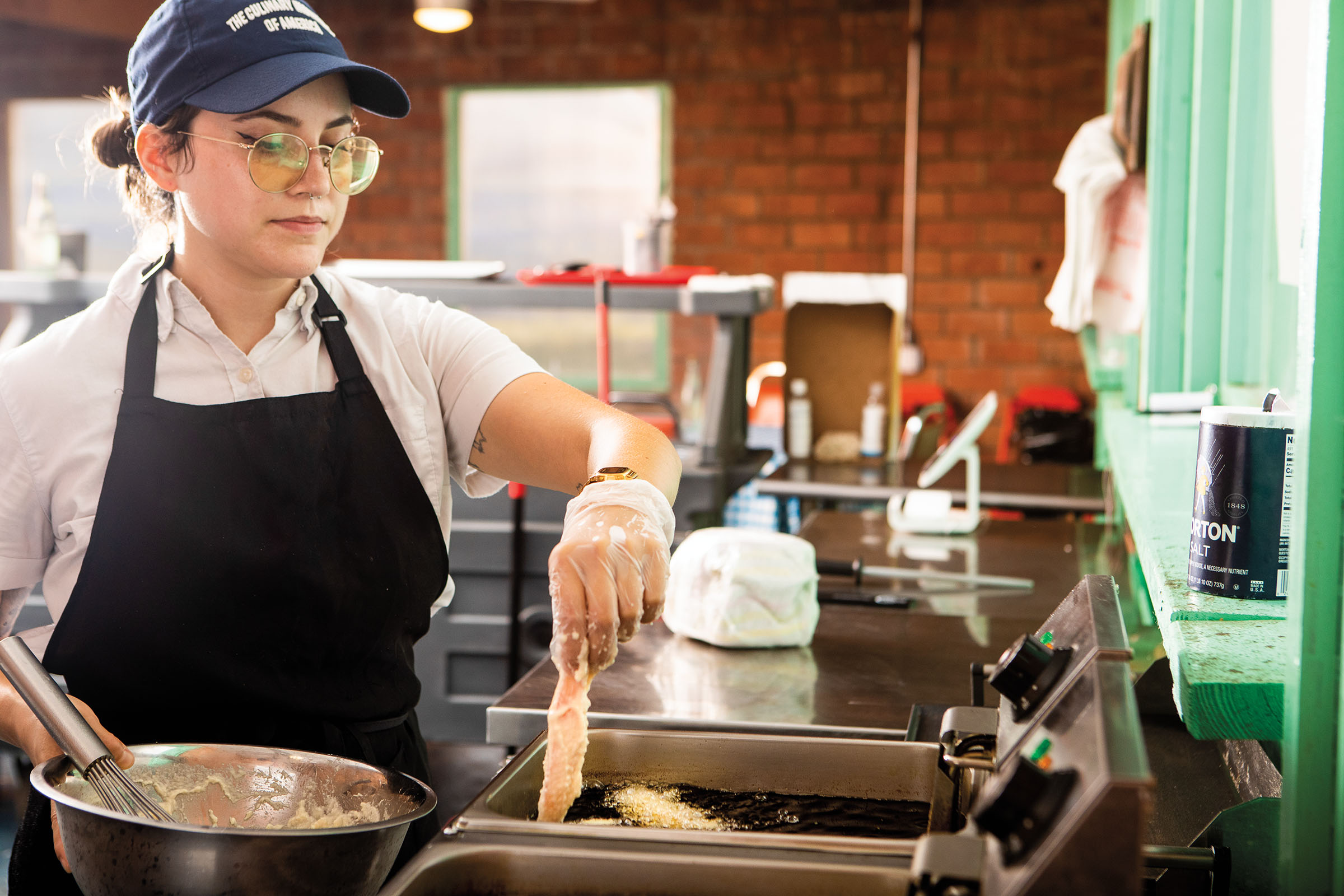 A woman in a blue baseball cap places fish fillets into a fryer