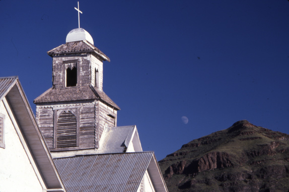 The top of an abandoned church in Shafter with a mountain and the moon in the background