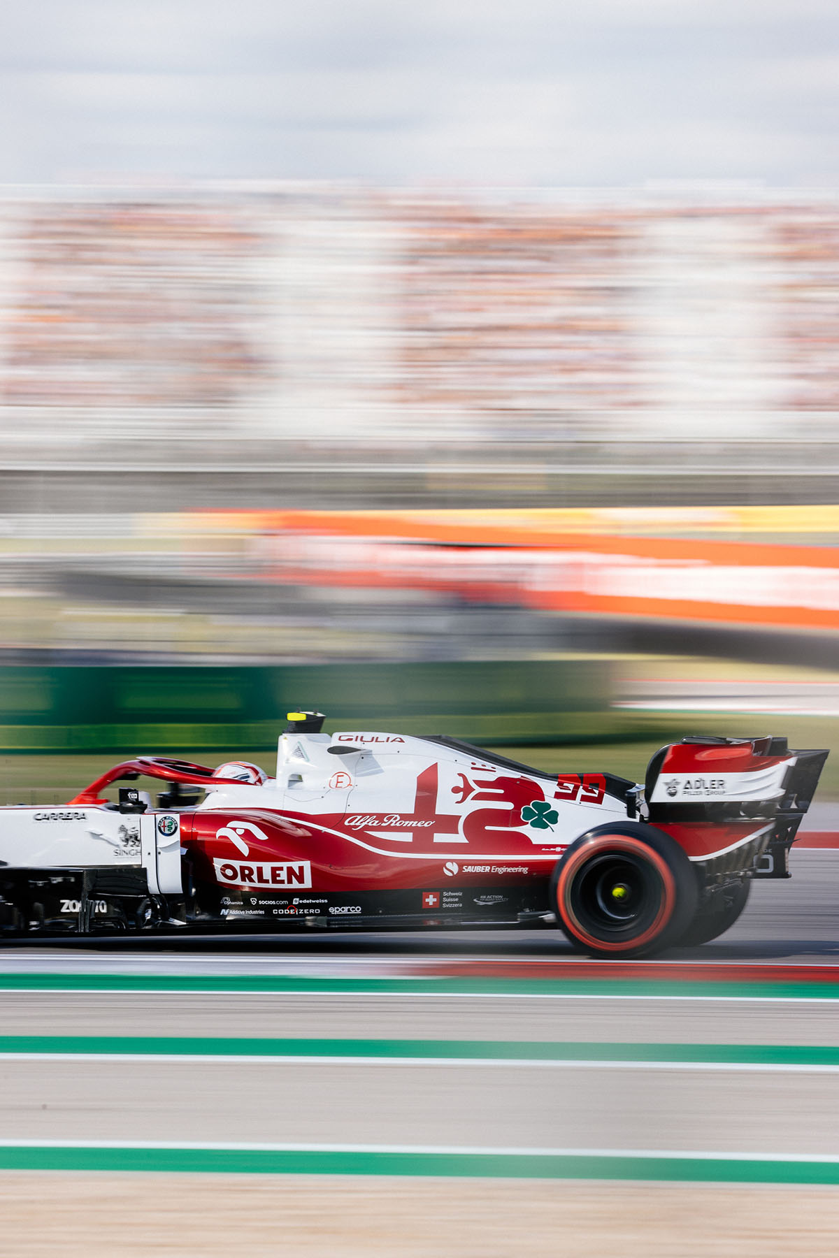 A red and white painted car passes quickly by a blurred background on a green-painted track