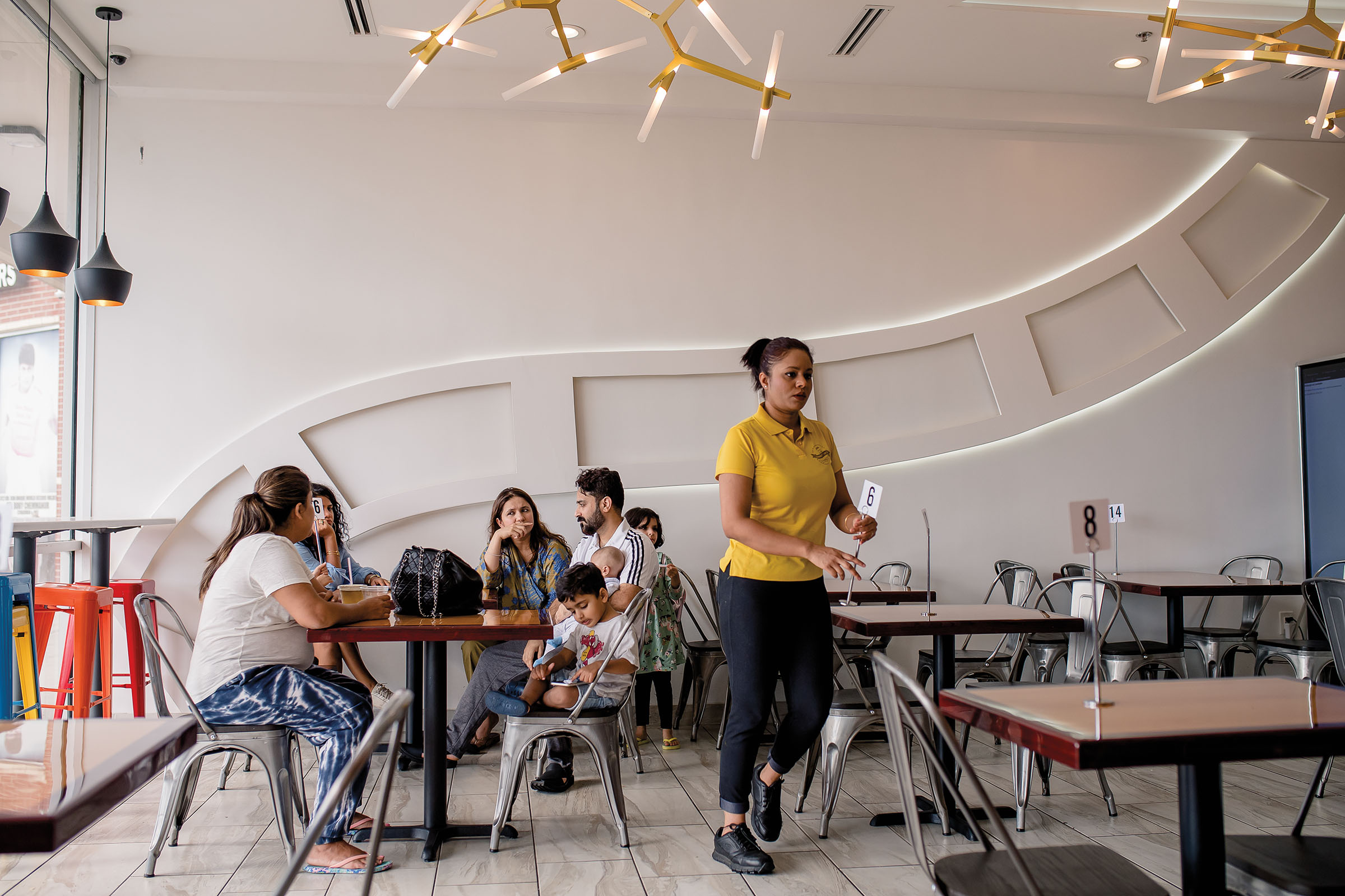 A group of people sit at a table in a restaurant with modern light fixtures and walls