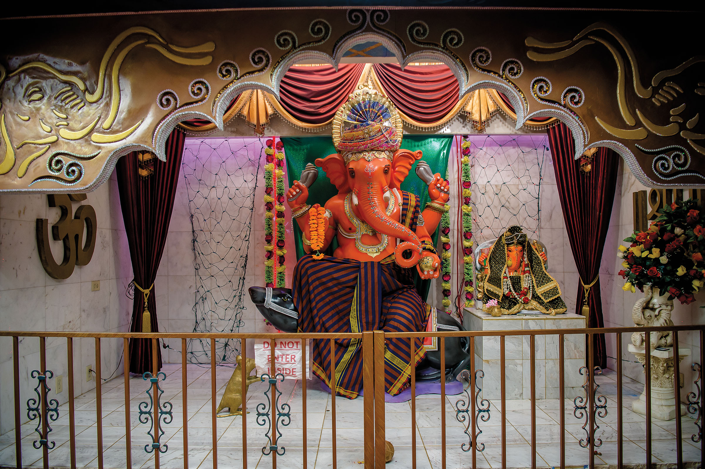 A brightly-colored elephant statue surrounded by gold dressings, flowers and a small gate
