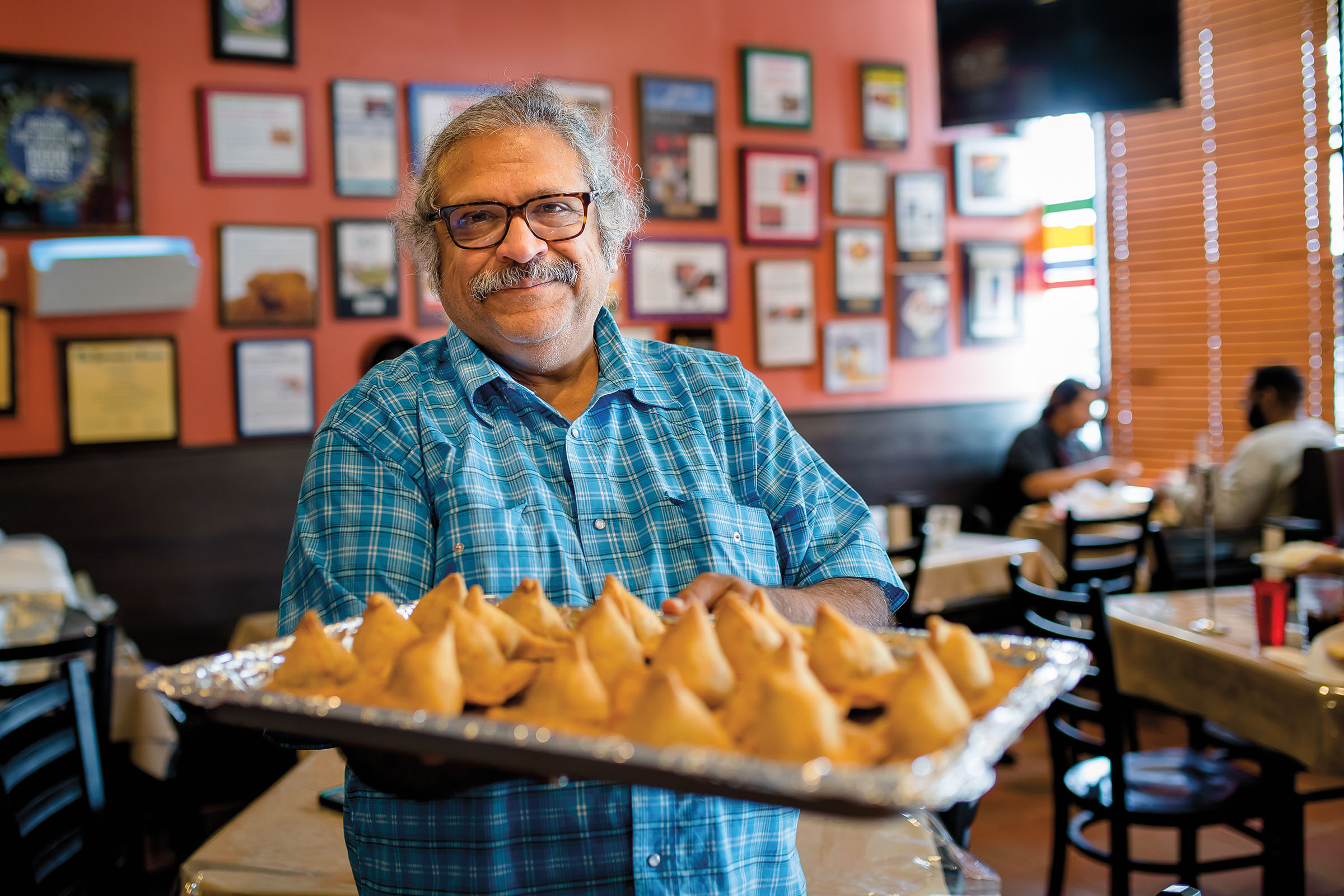 A man in a blue shirt and glasses holds out a tray of golden pastries