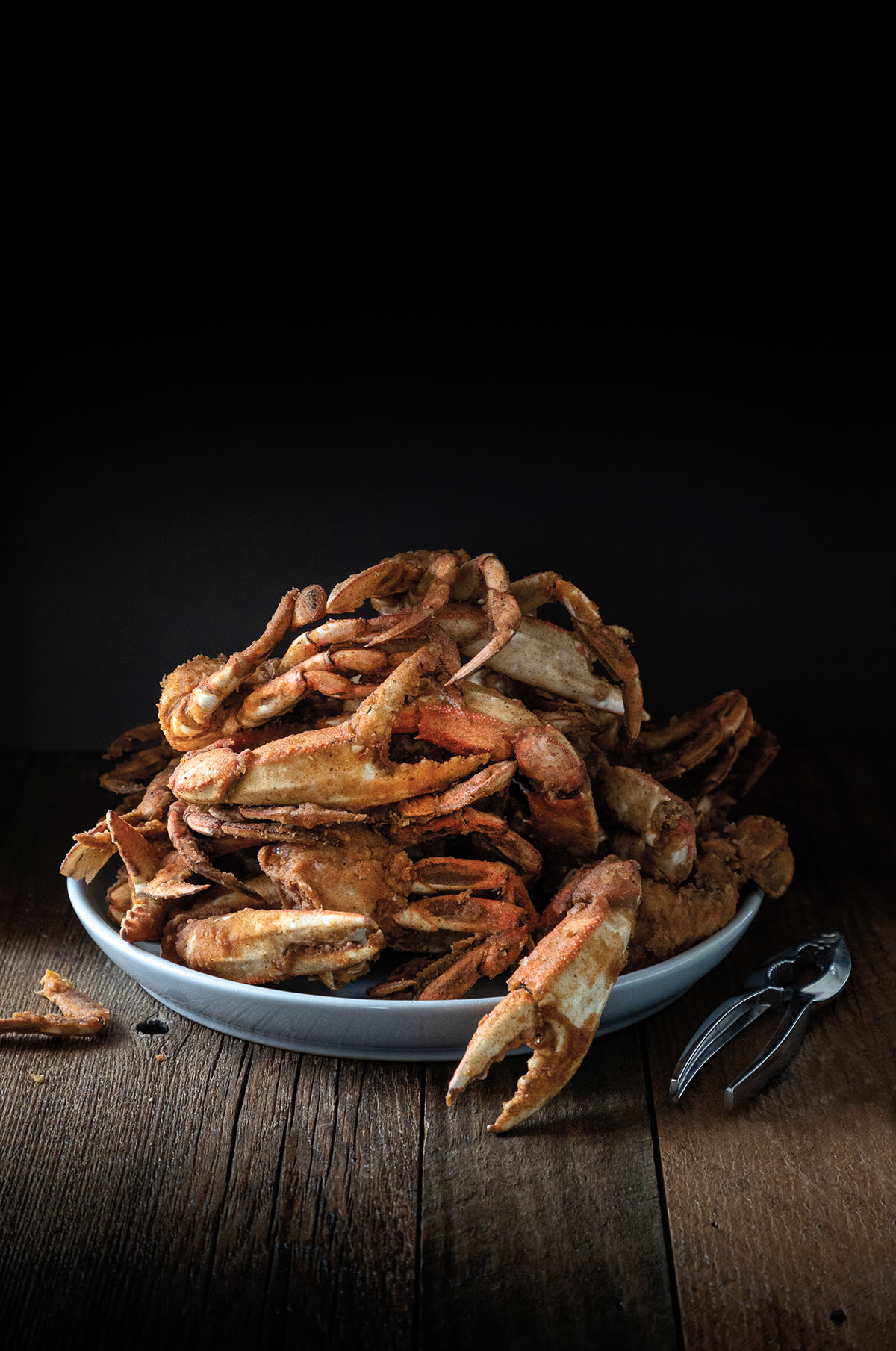 A pile of reddish-brown roasted crabs on a platter in front of a black background