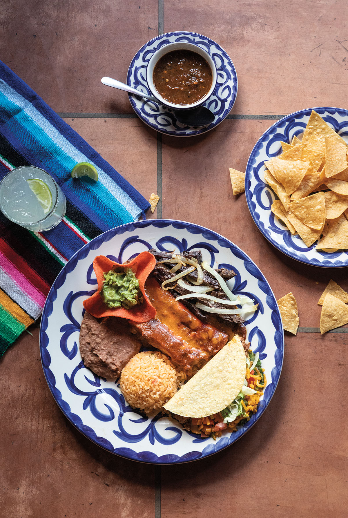 An overhead view of enchiladas on a blue plate, chips and salsa