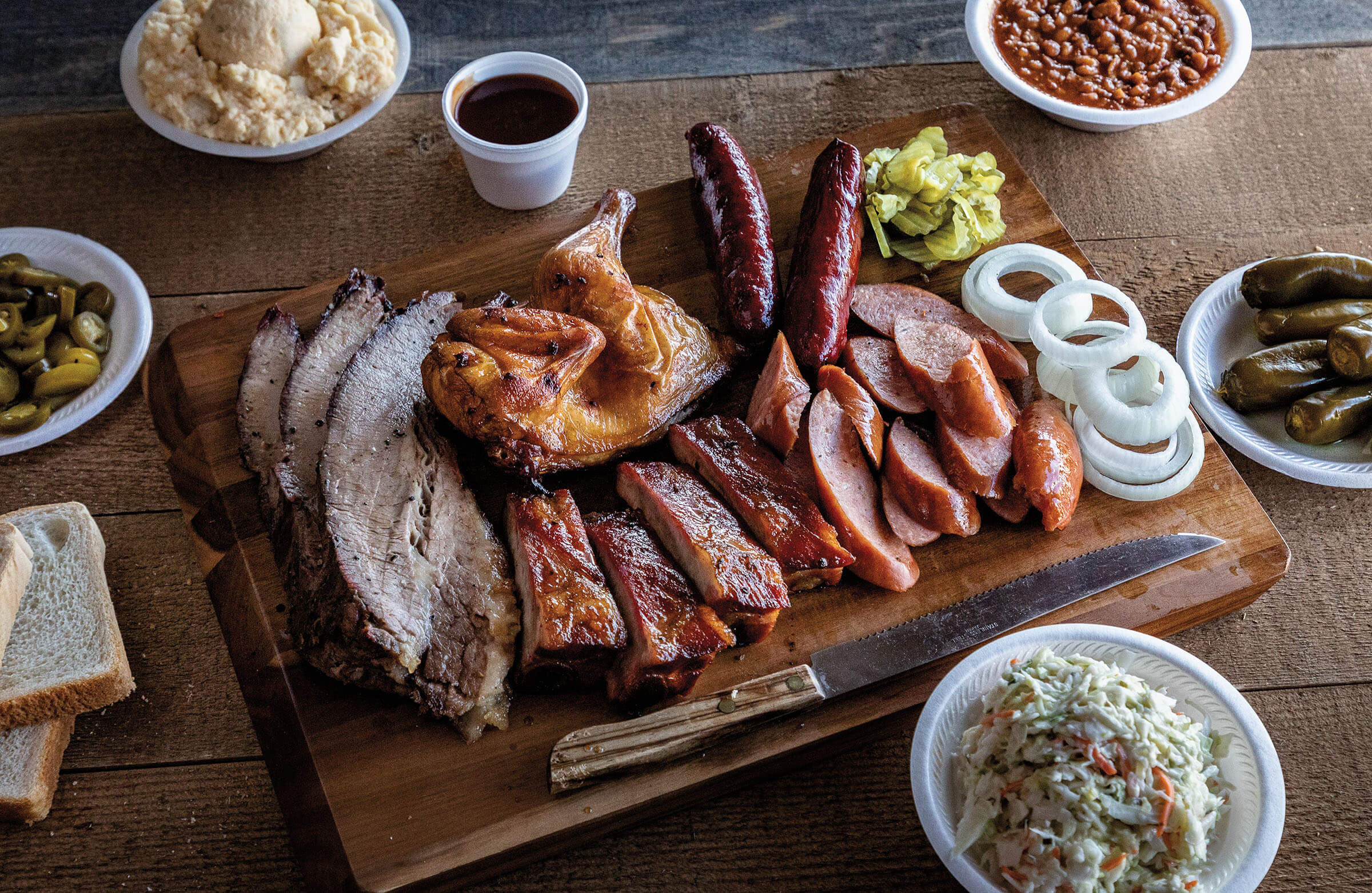 An overhead view of a slection of barbecue, including brisket, chicken, sausage, and sides on a wooden tray