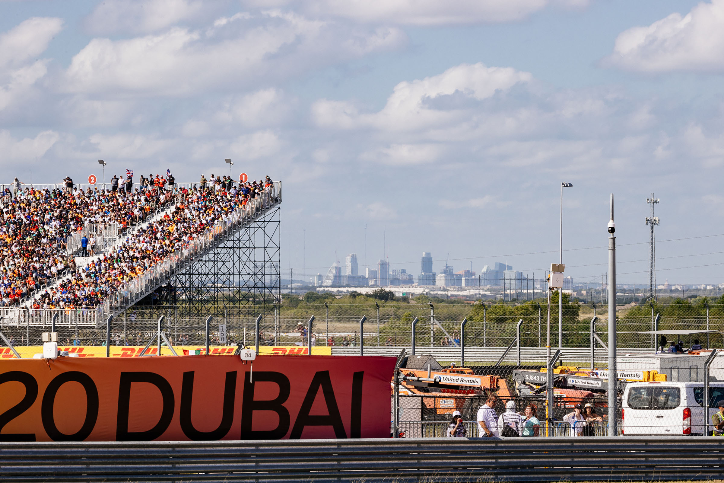 The Austin skyline peeks above the trees next to stands full of people in brightly colored attire and a banner reading 'DUBAI'