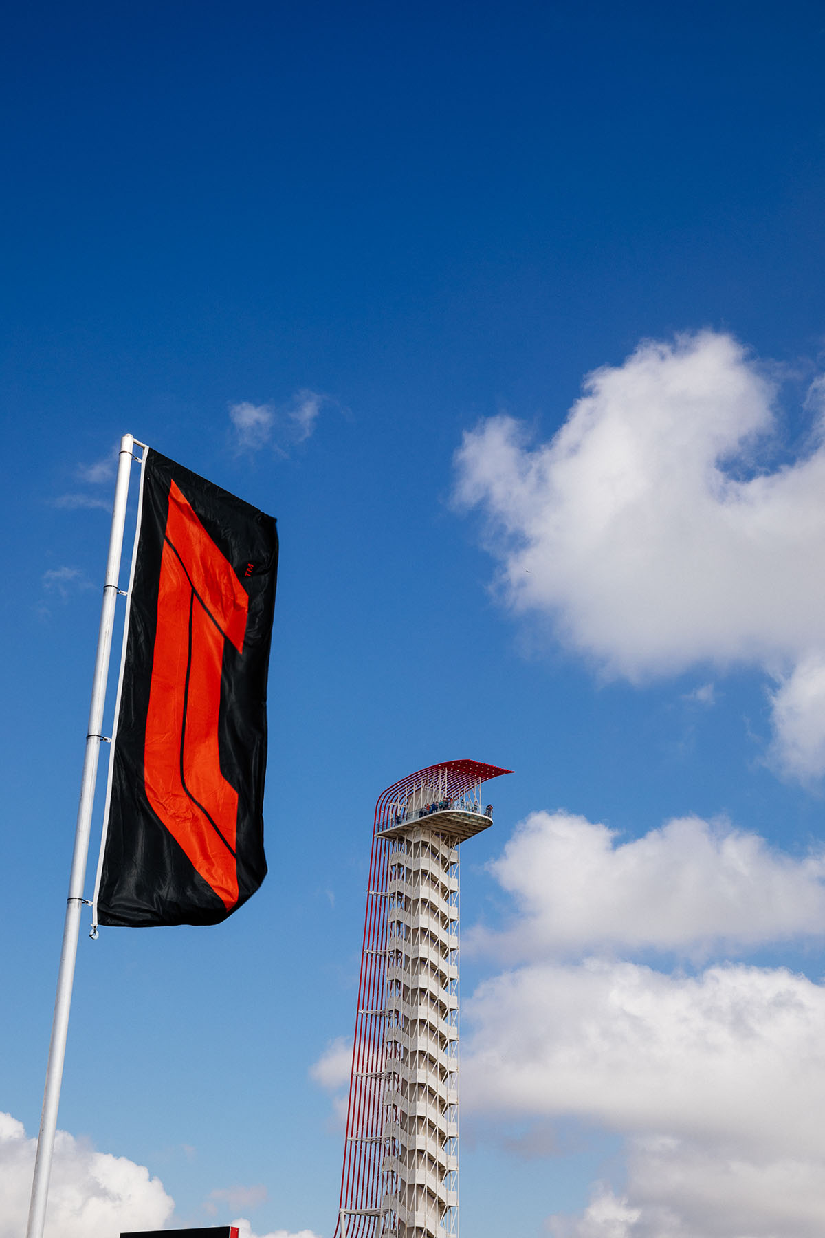 A red flag in front of a tall white and red tower in front of bright blue sky