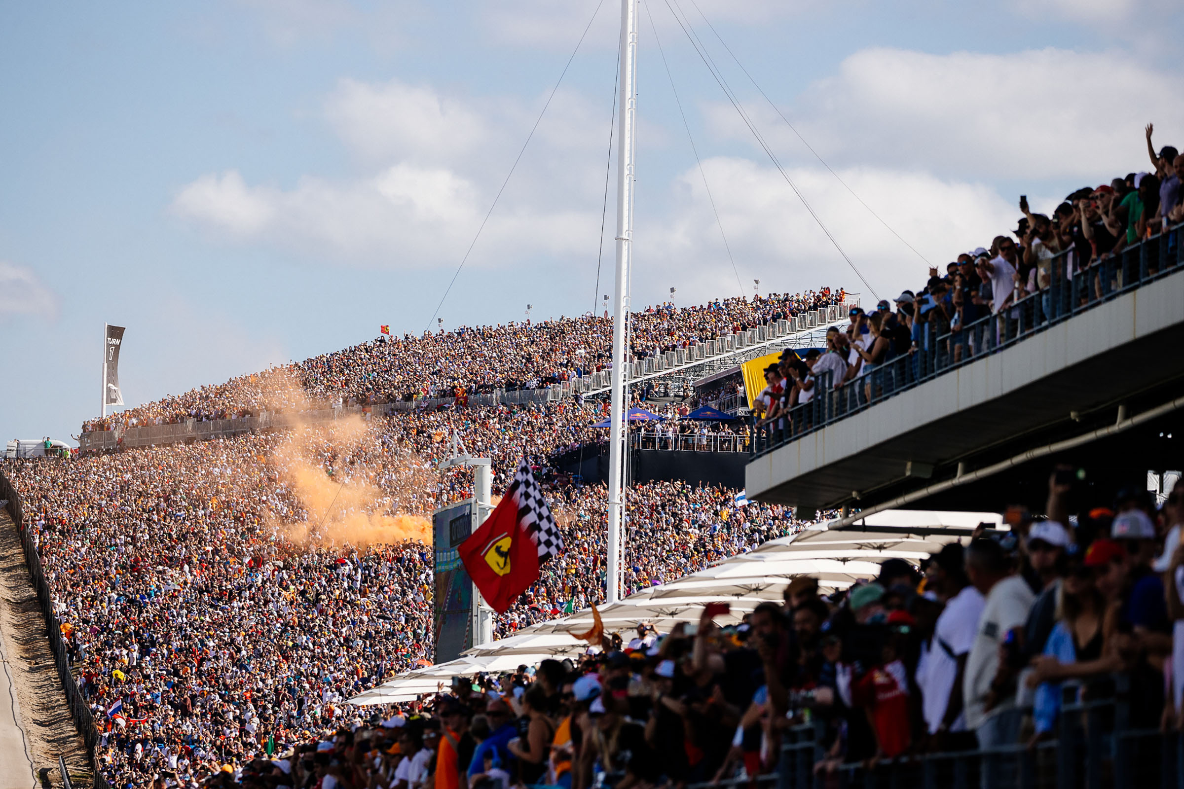 A wide view of the completely full stands, with flags waving in the area and orange smoke bombs being ignited
