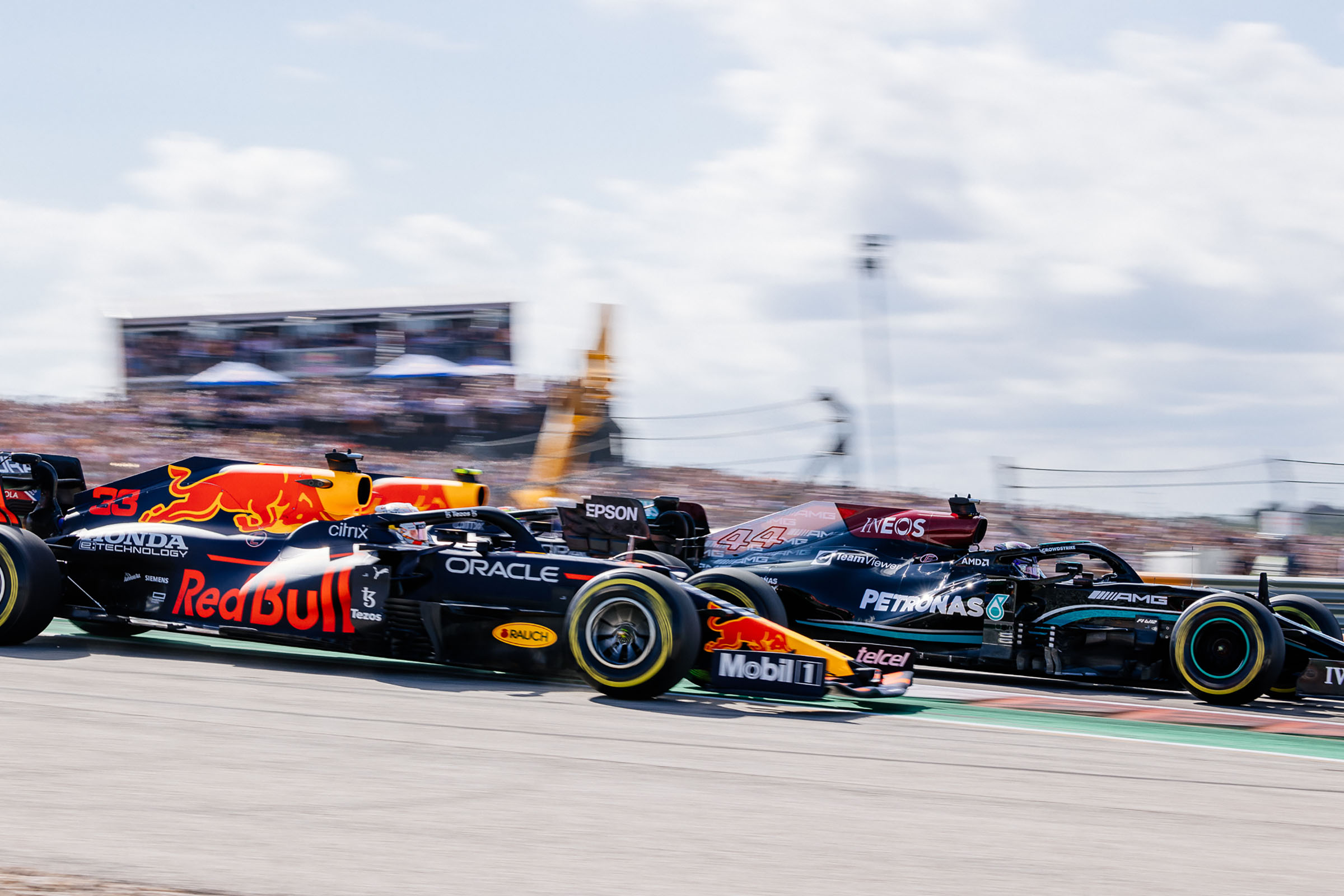 A black and yellow car with the RedBull logo moves past a black and teal car reading Petronas