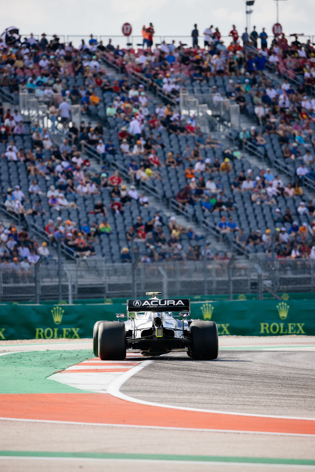 A car with large black wheels and a black sign reading 'Acura' comes down the racetrack