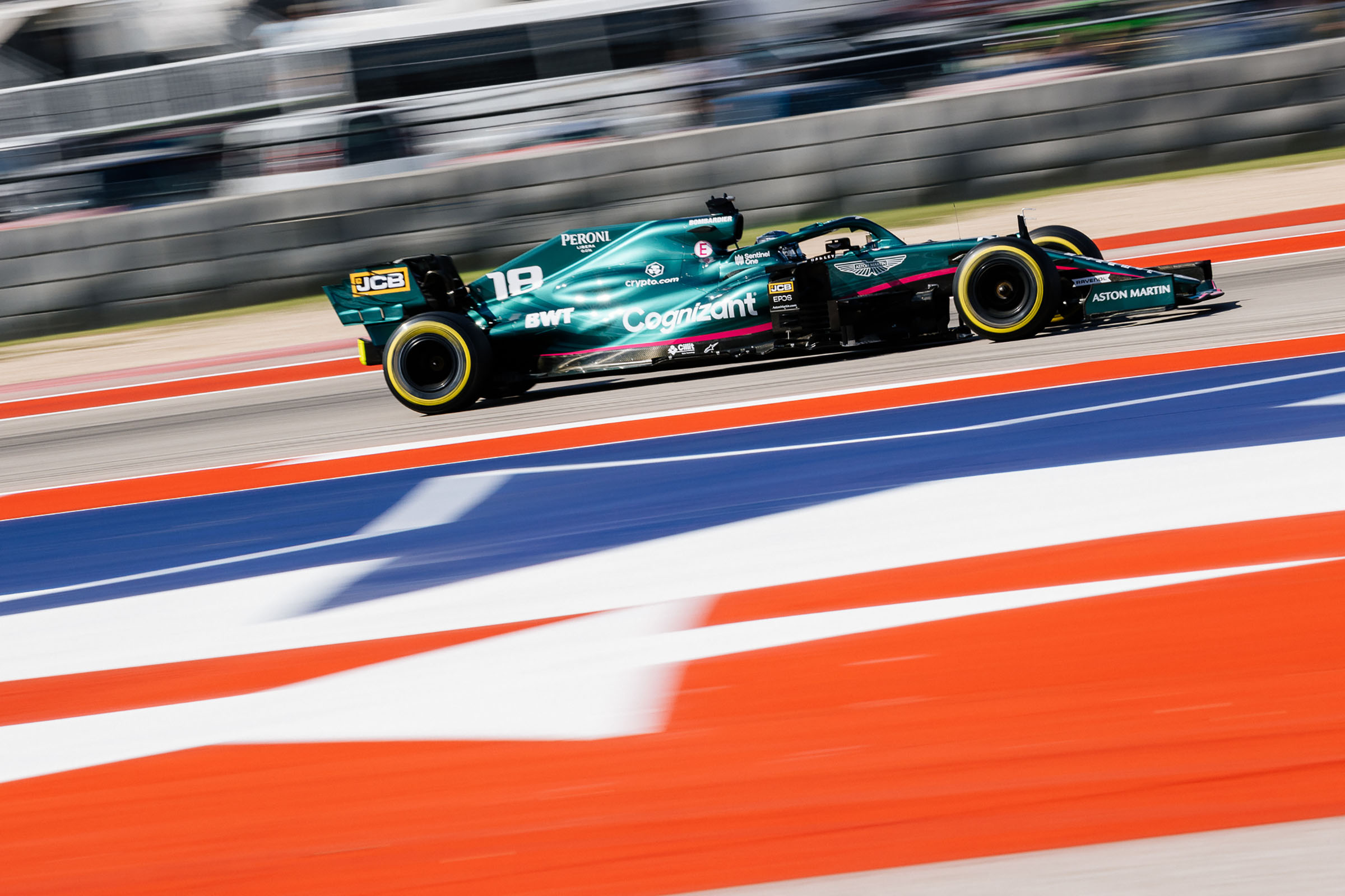 A green car with yellow-rimmed tires drives past red, white and blue painted asphalt