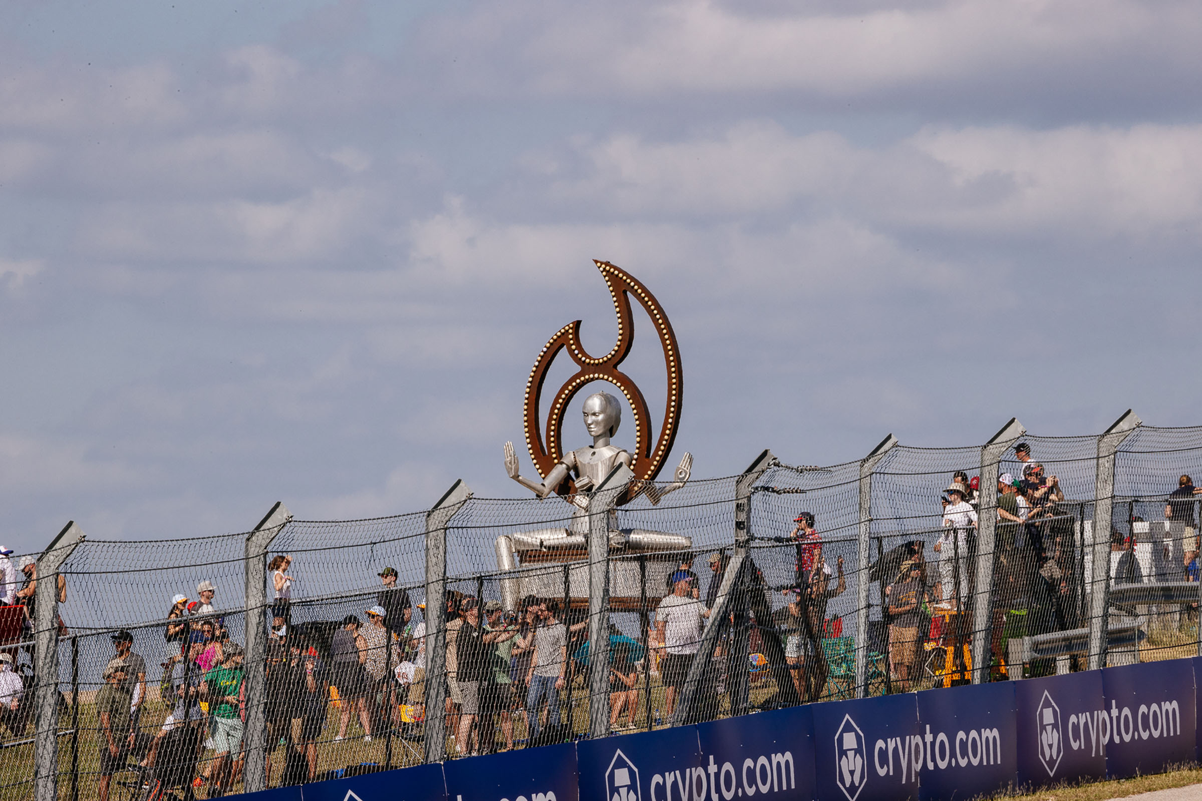 A silver statue of a woman surrounded by a brown flame holds her hands up as people mill about