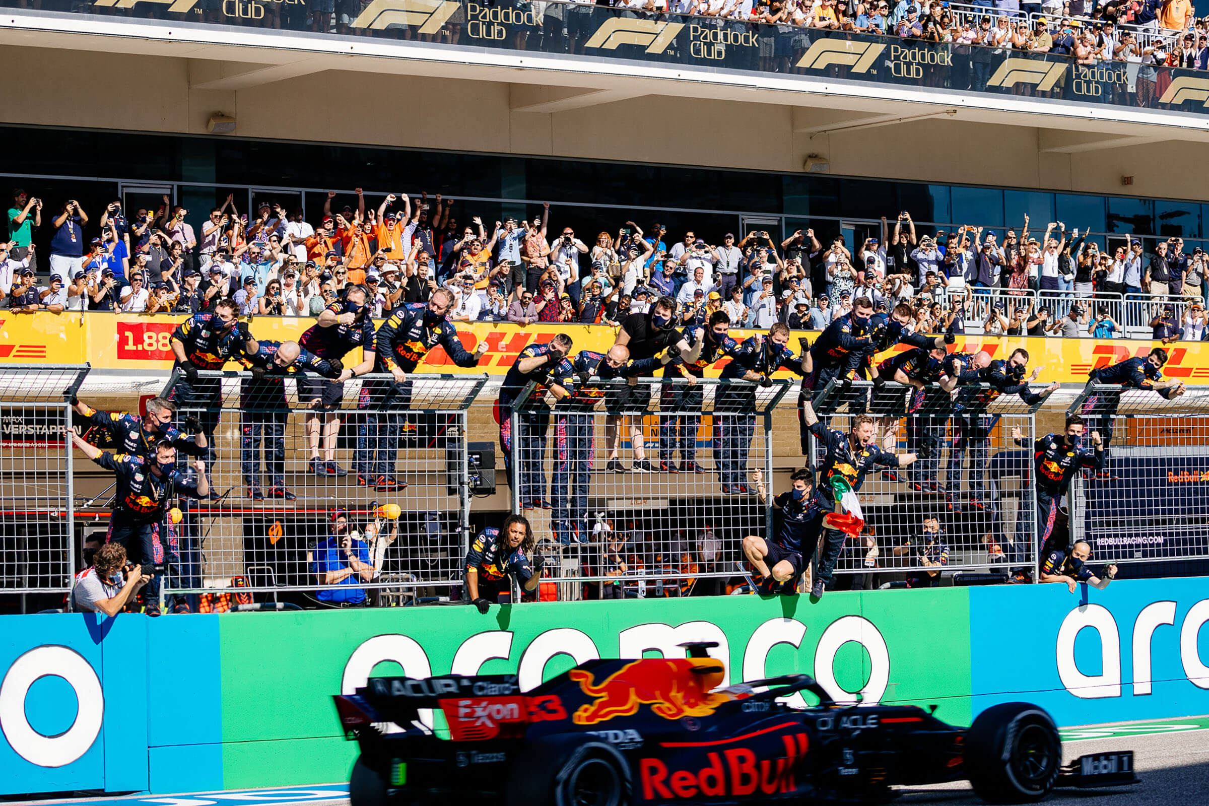 Men in race crew uniforms jump down from a fence to celebrate