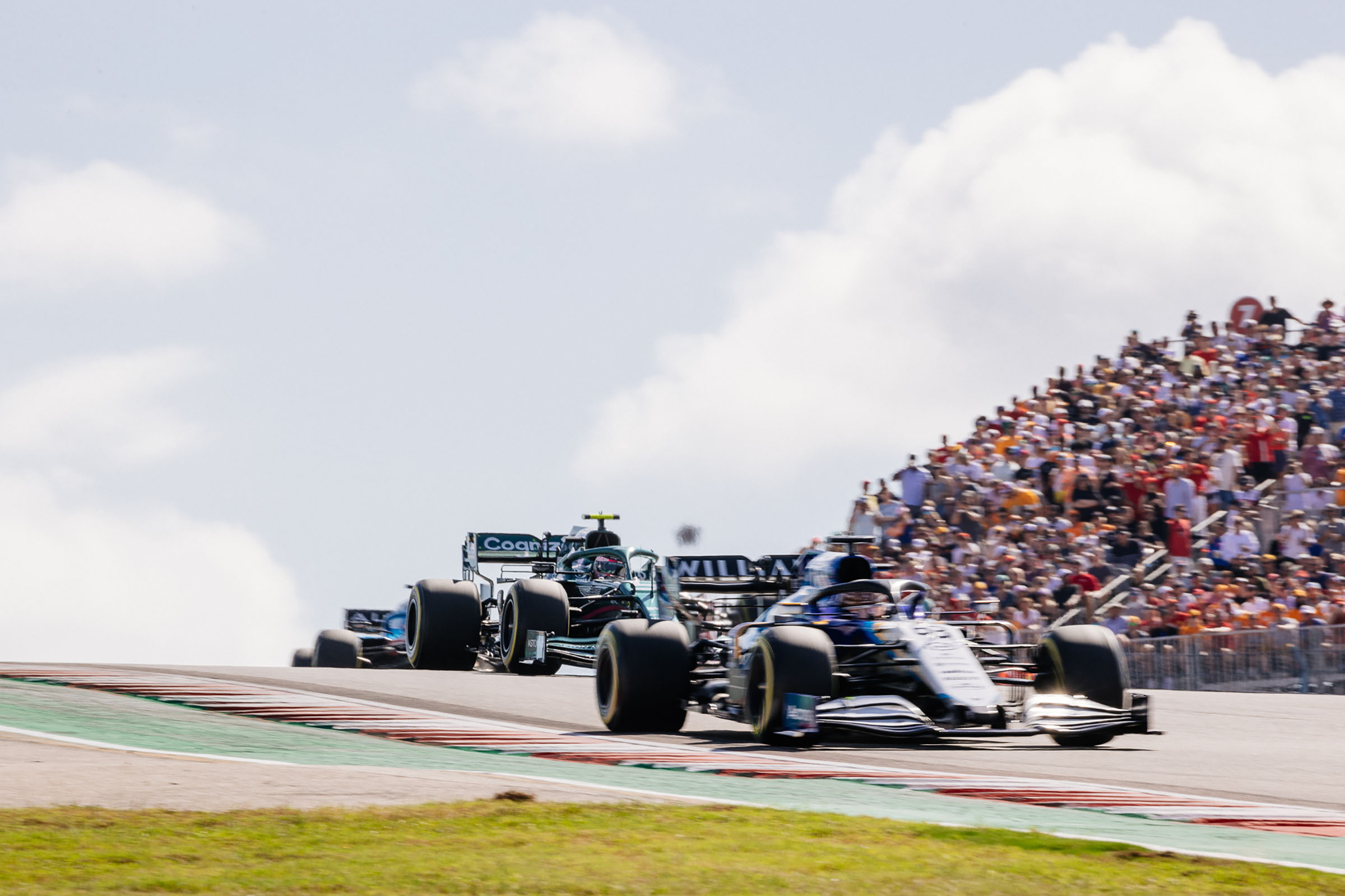 Spectators look on as a group of cars with large tires drive past