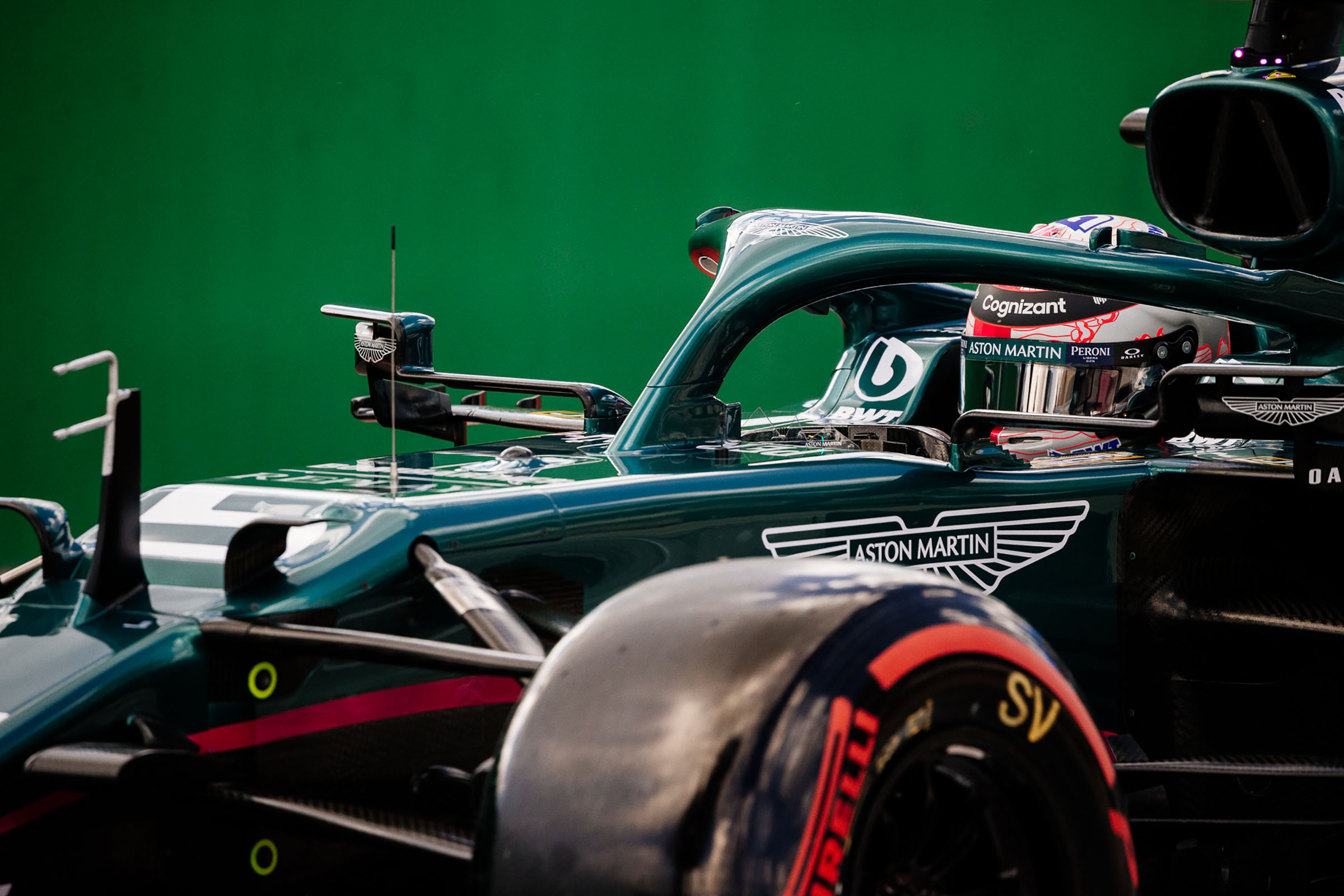 A detailed photo of a man in a brightly painted racing helmet inside of a green car with 'Aston Martin' painted on the side