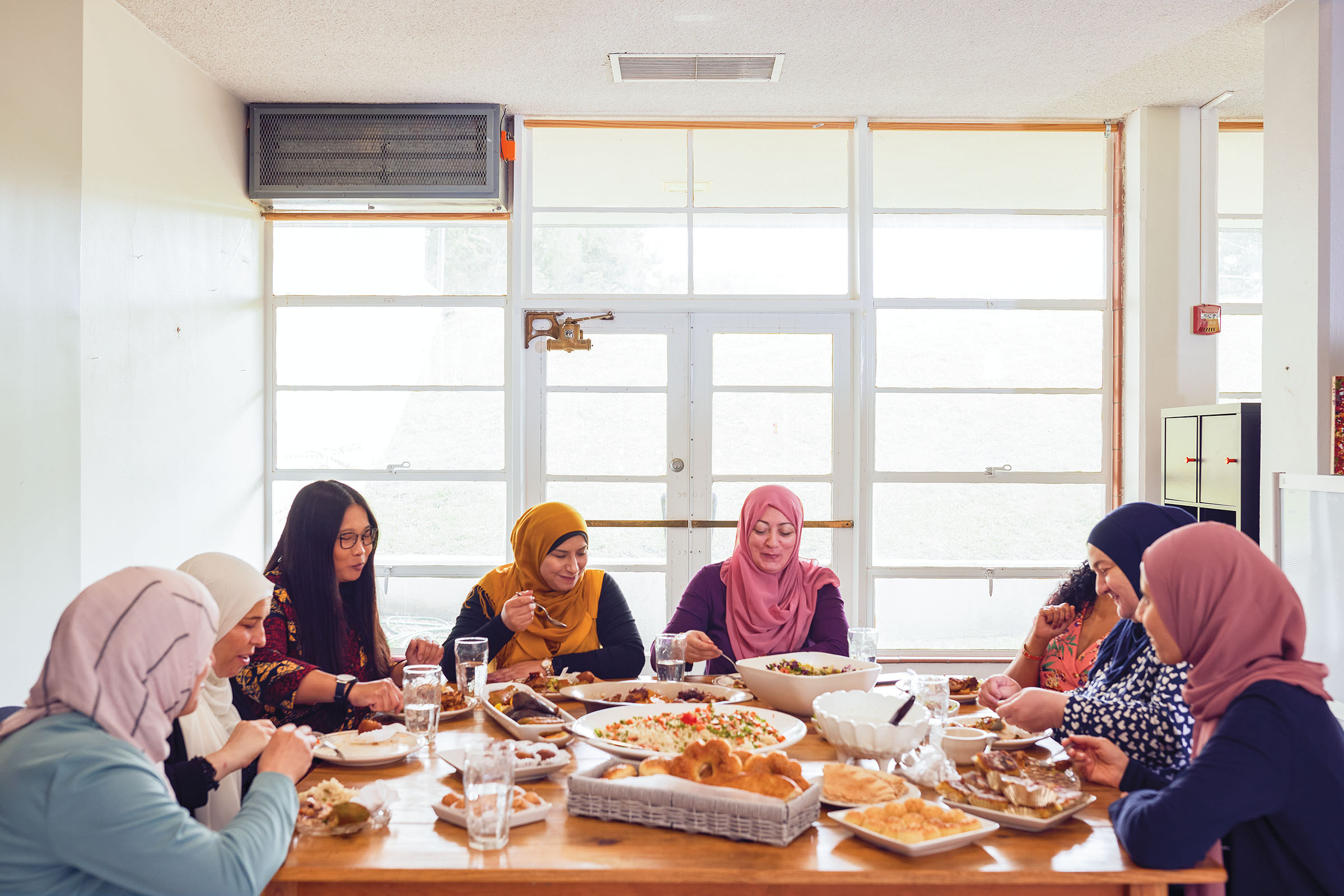 A group of women sit around a well-lit table in front of windows