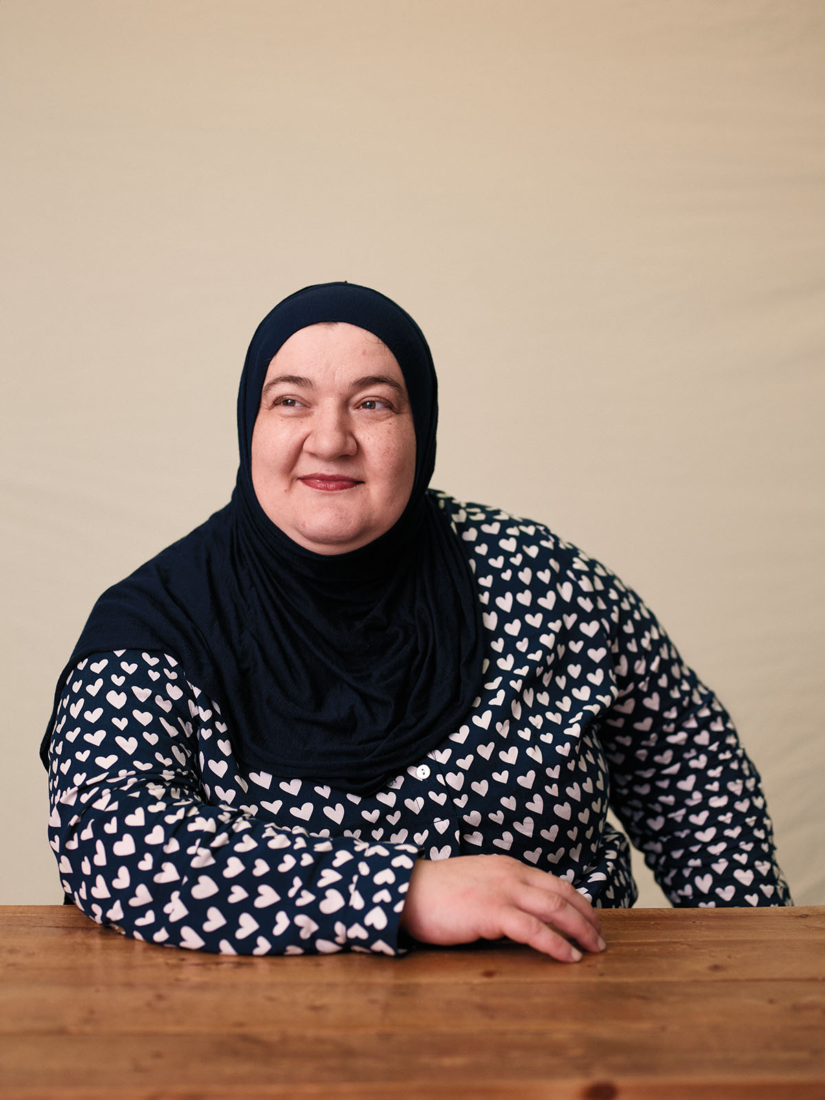 A woman in a black hijab and black and white patterned shirt looks into the distance past the camera