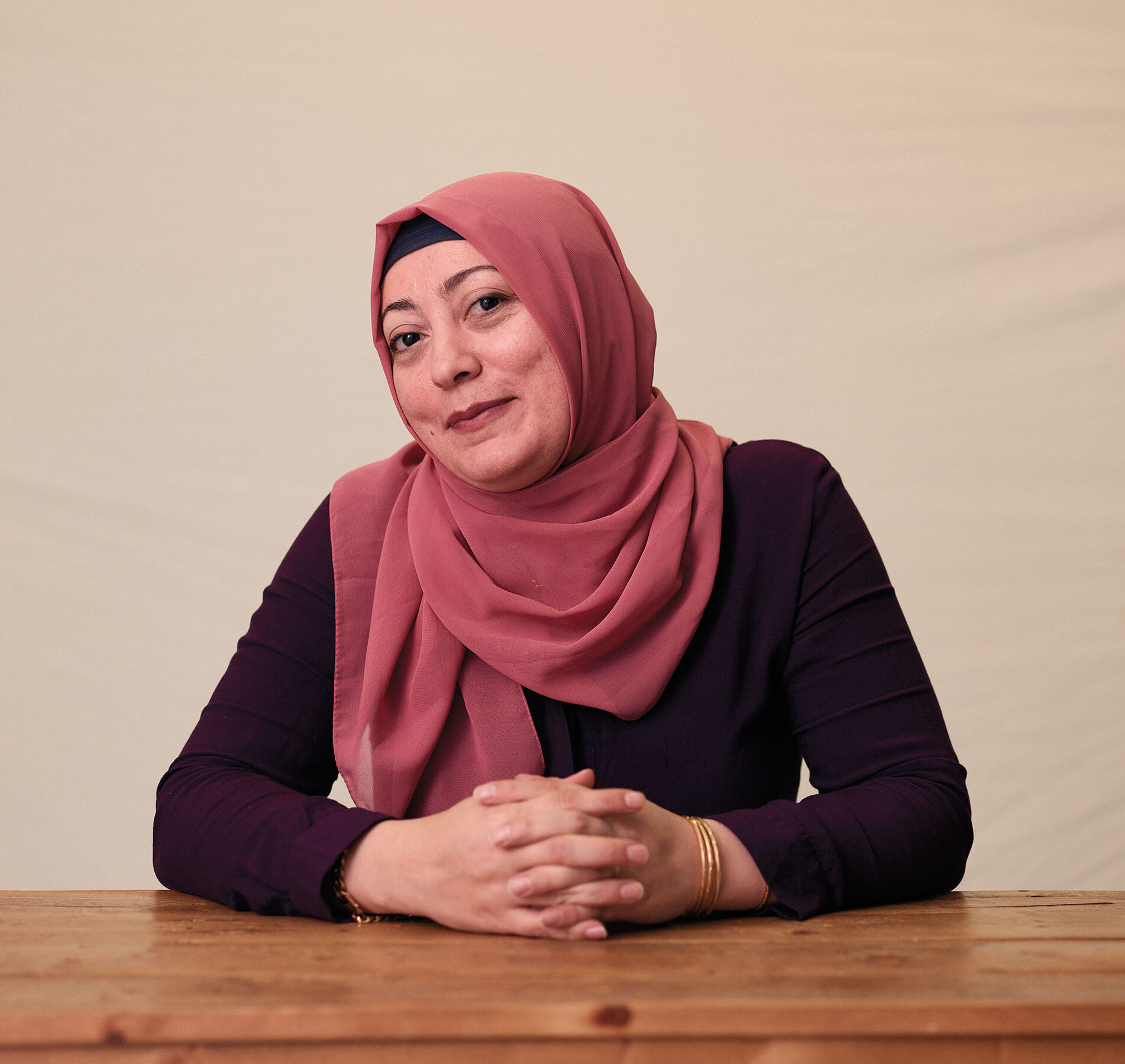 A woman in a pink hijab smiles with her head tilted toward the camera
