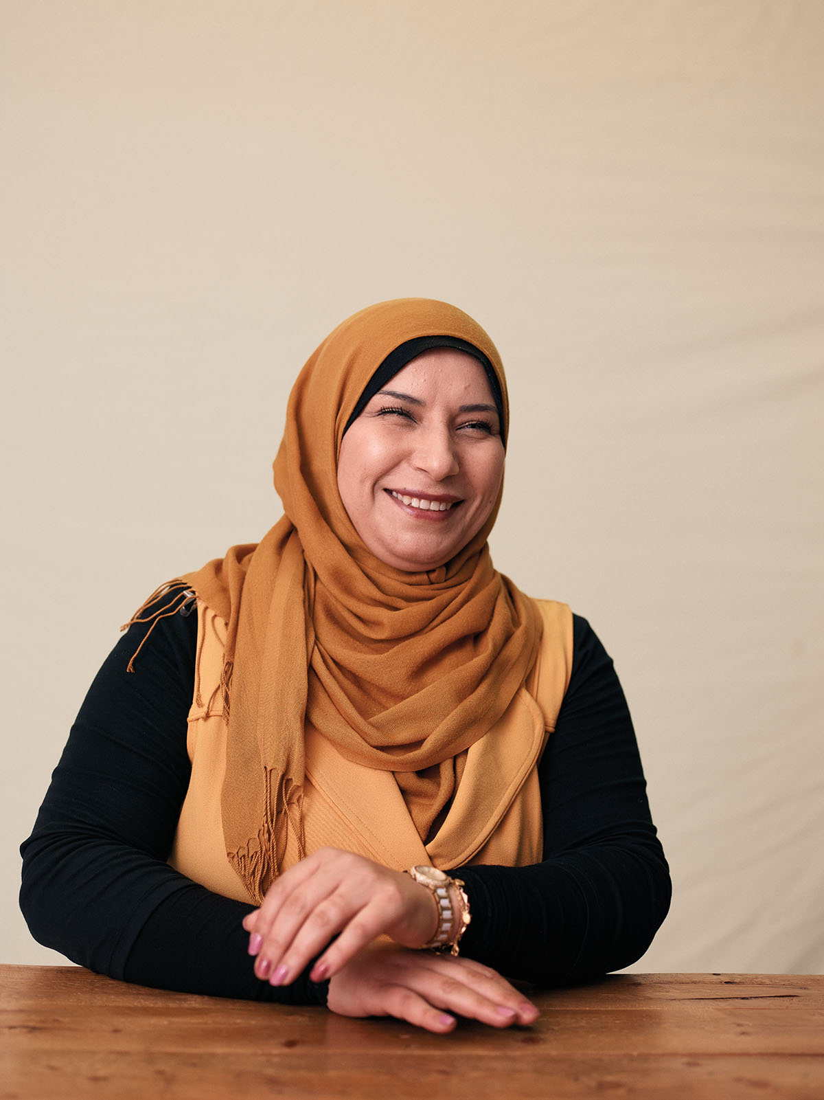 A woman in a gold-colored hijab smiles and moves to fold her hands