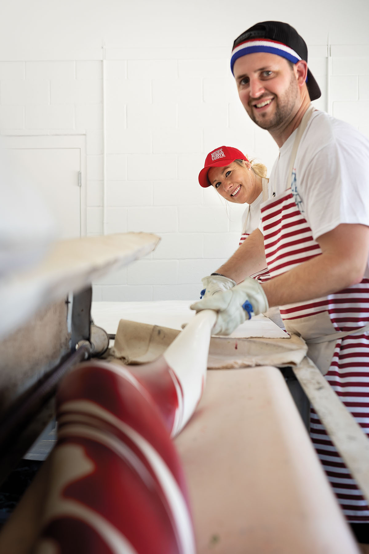 Two people lean over a counter wearing brightly-colored aprons