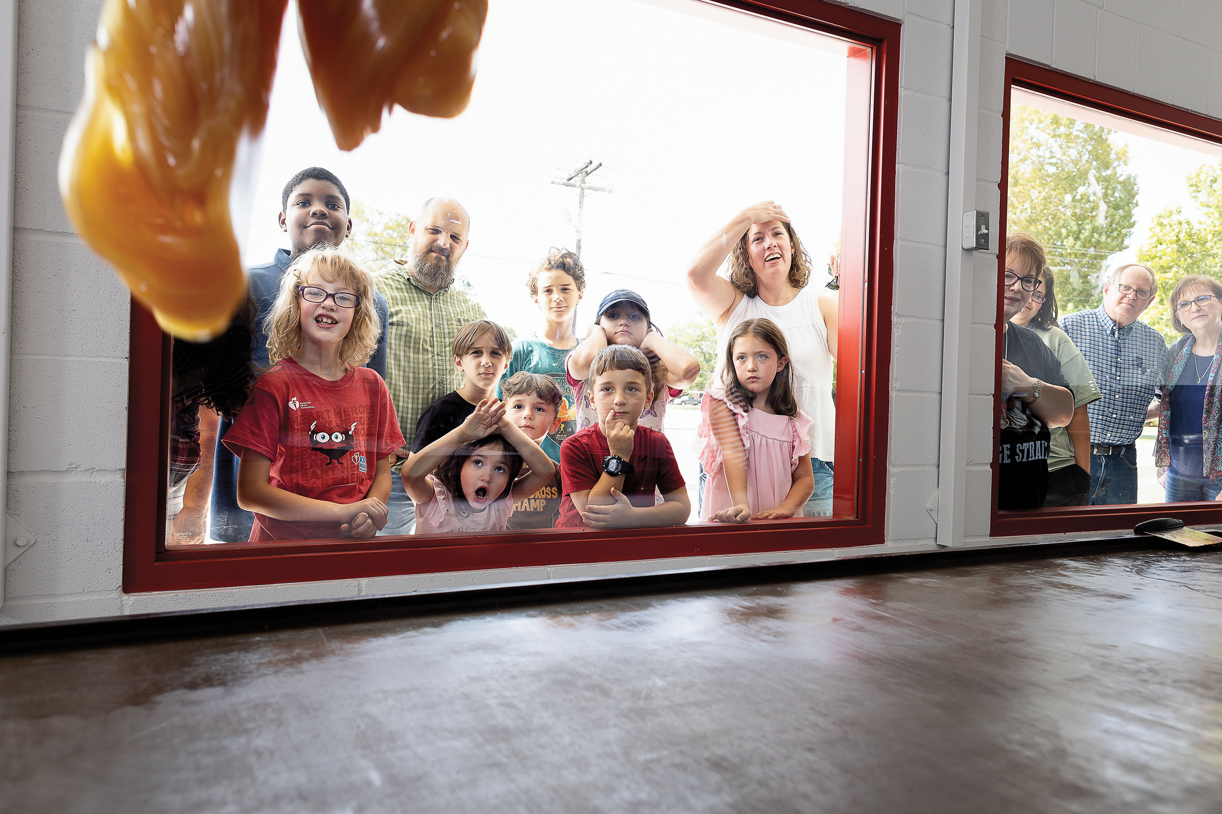 A group of people, mostly young, look through the shop window at candy being made