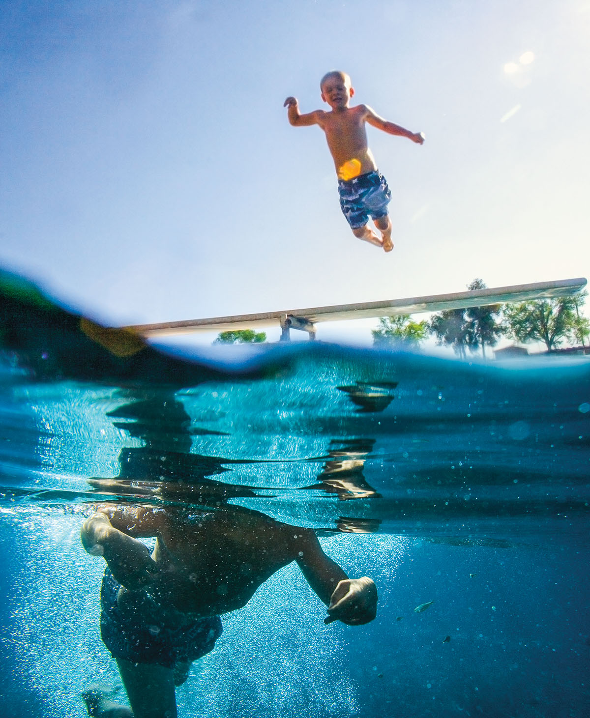 A young person in a blue swimsuit jumps into the clear blue water of Balmorhea pool