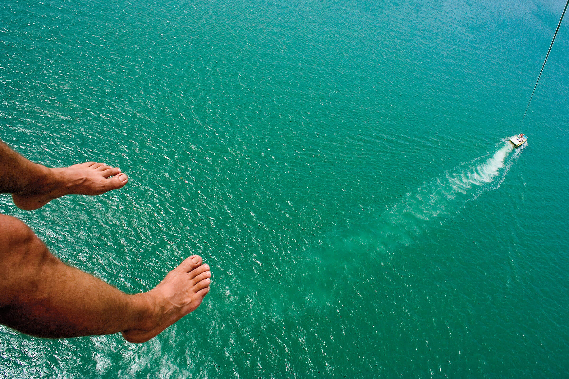 Two feet dangle over bright blue-green water with a boat in the distance